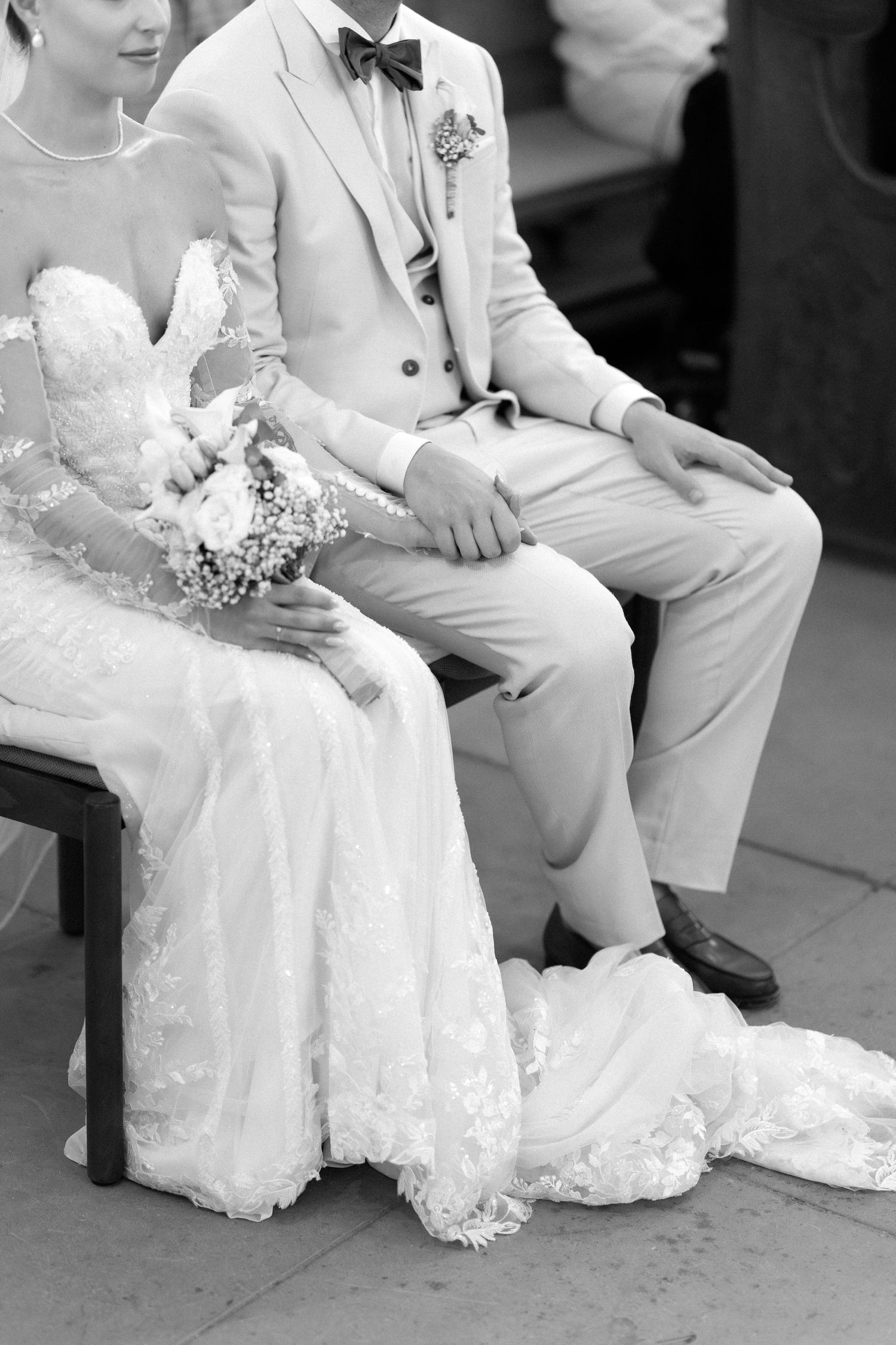 A black and white wedding photo shows a couple sitting together with the bride's lace dress elegantly draped.