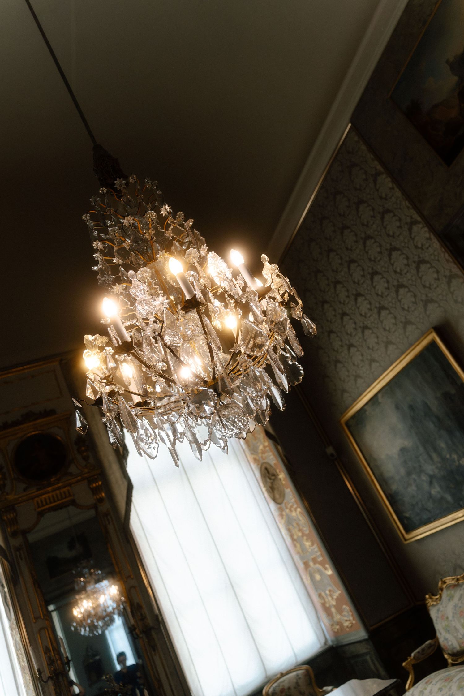 Crystal chandeliers hanging from ornate ceiling in an elegant interior space.