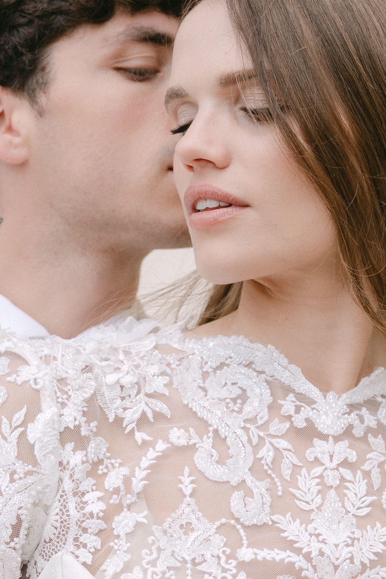 Romantic close-up portrait showing tender intimacy between couple with woman wearing delicate white lace dress. Villa Mosconi Bertani