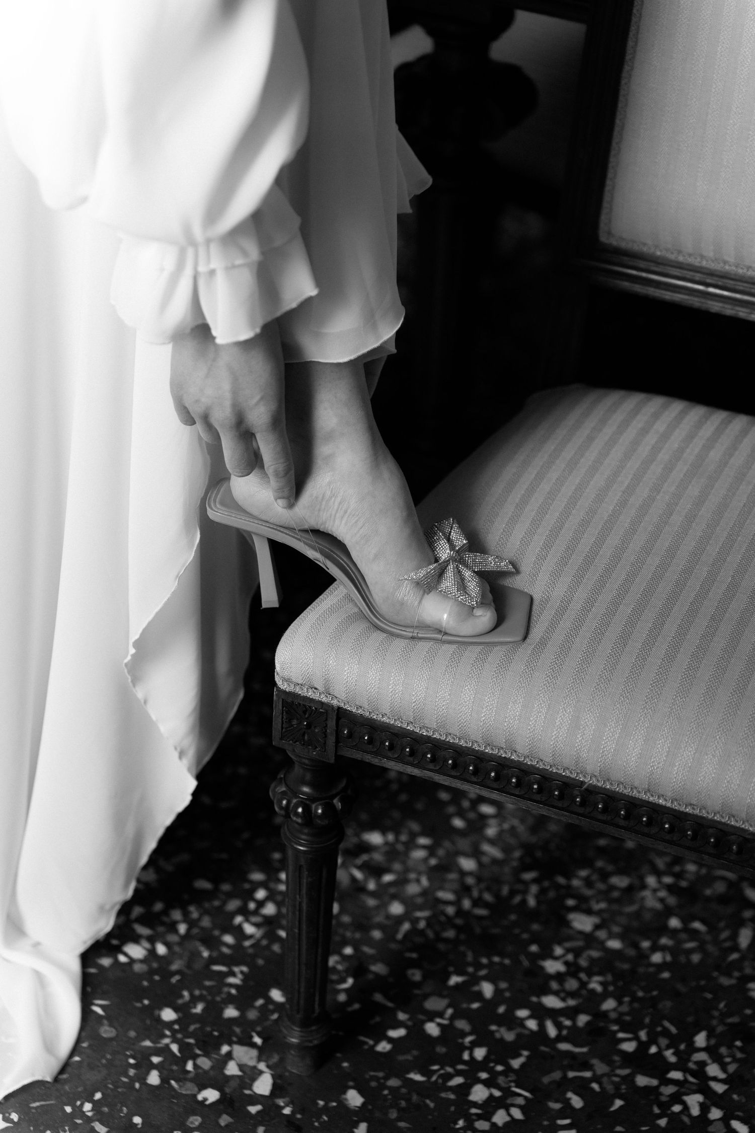 Black and white image showing feet in white shoes on a patterned carpet at what appears to be a formal event. Wedding Verona