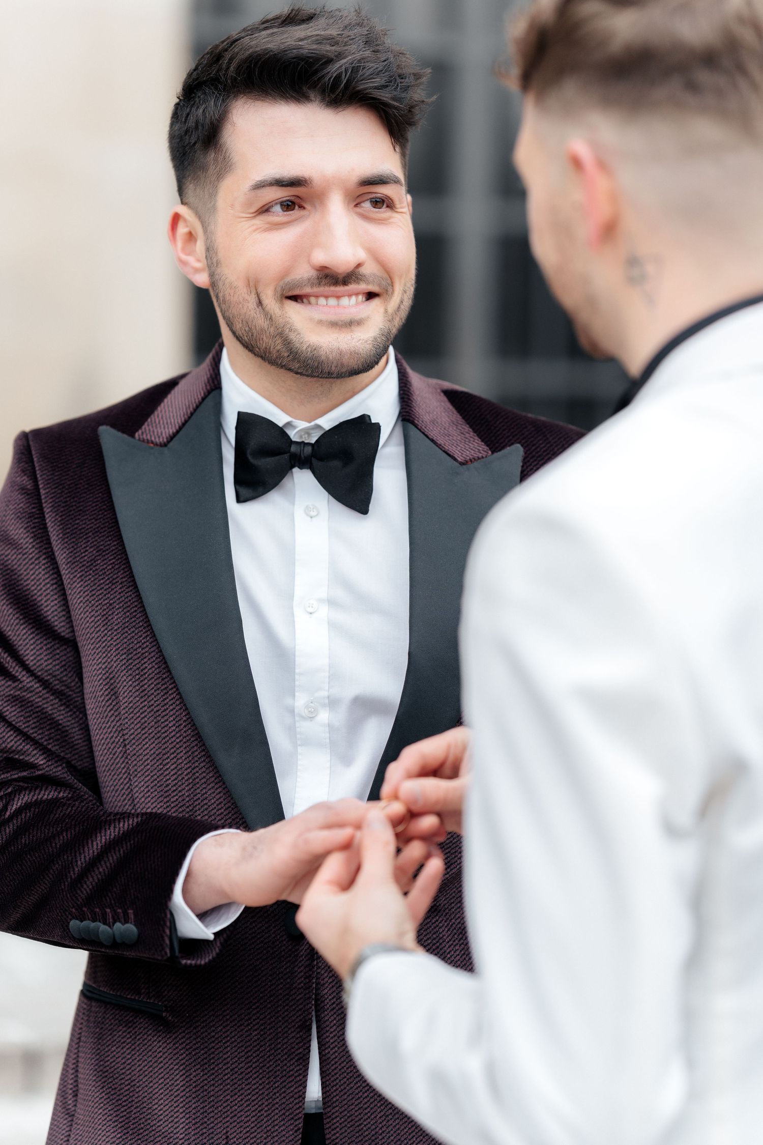 Two people in formal tuxedos share an intimate moment during what appears to be a wedding ceremony.