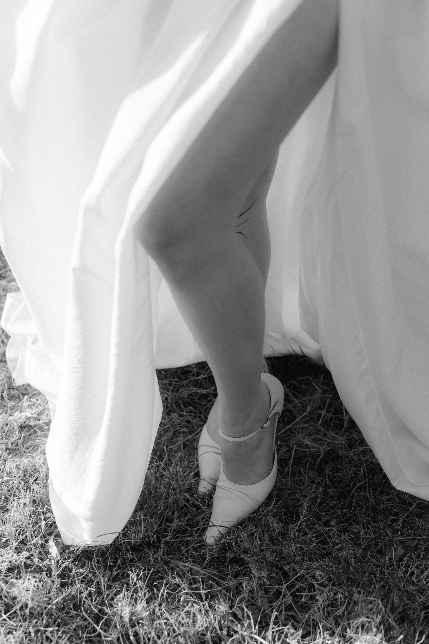 Close-up view of feet wearing white ballet flats beneath a flowing white dress on grass.