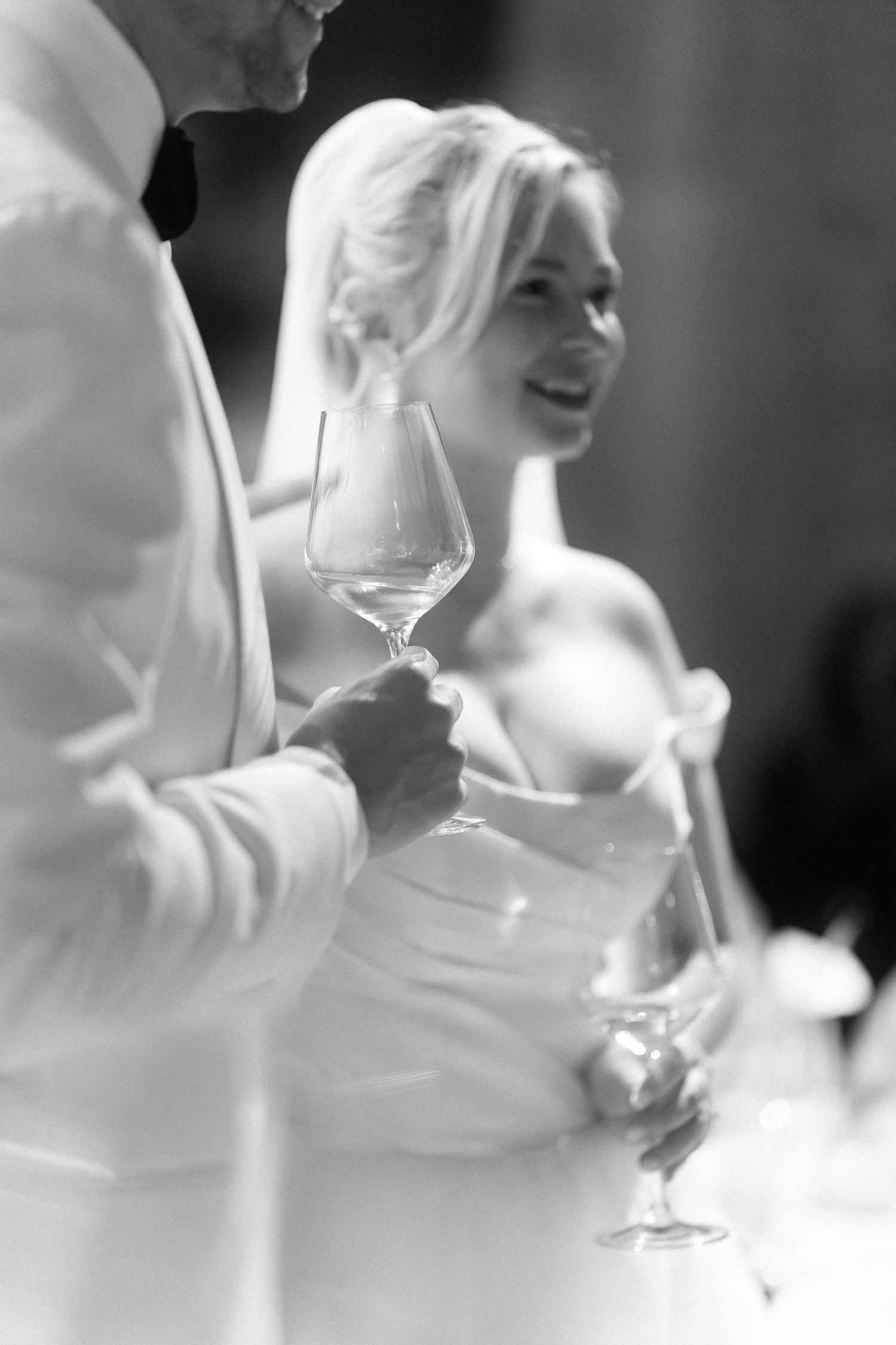 Black and white photo of wine glasses being held at an elegant event with white formal attire.