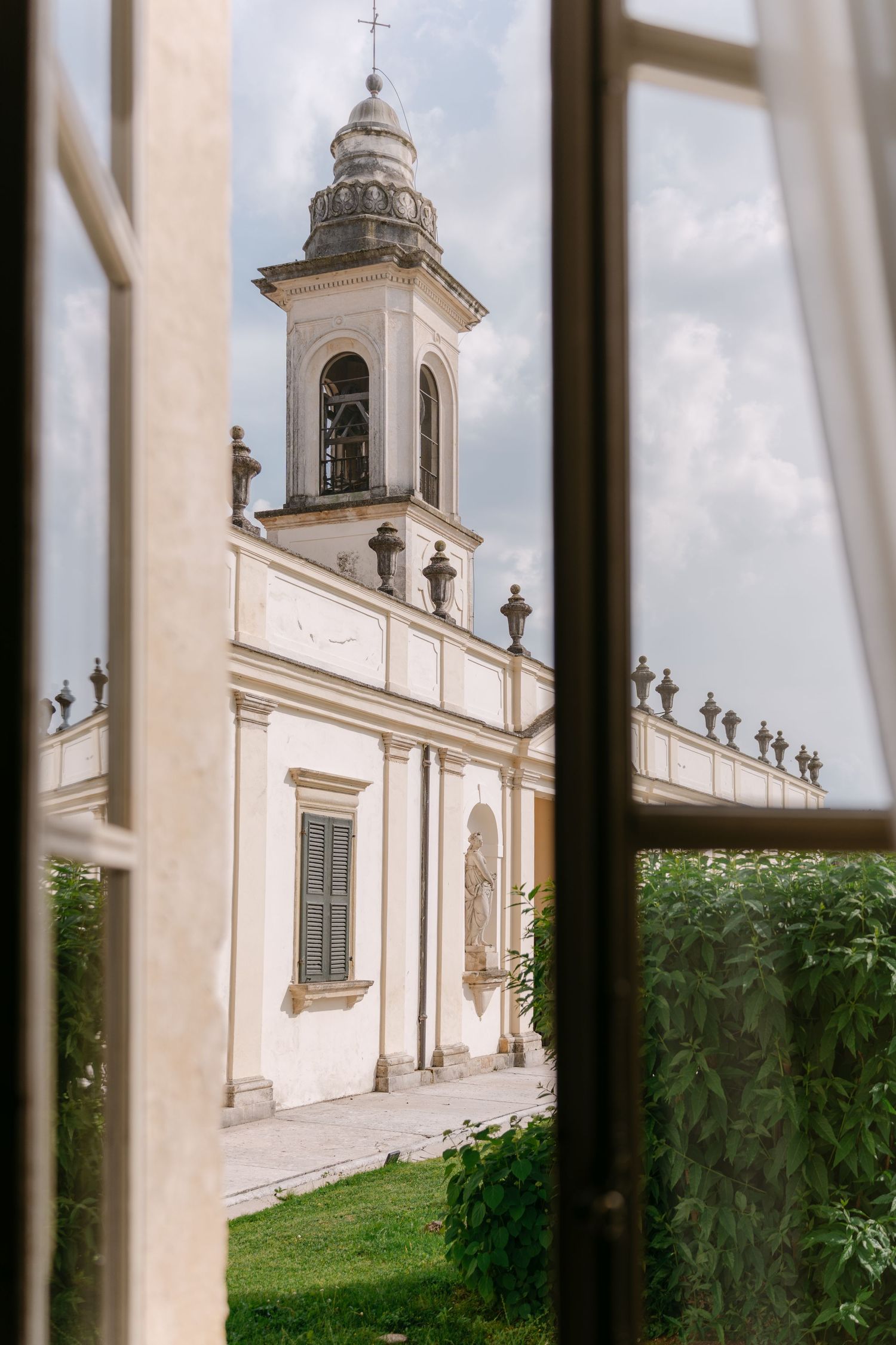 View through a window of a white church with bell tower and ornate decorative elements on a grassy lawn. Villa Mosconi Bertani
