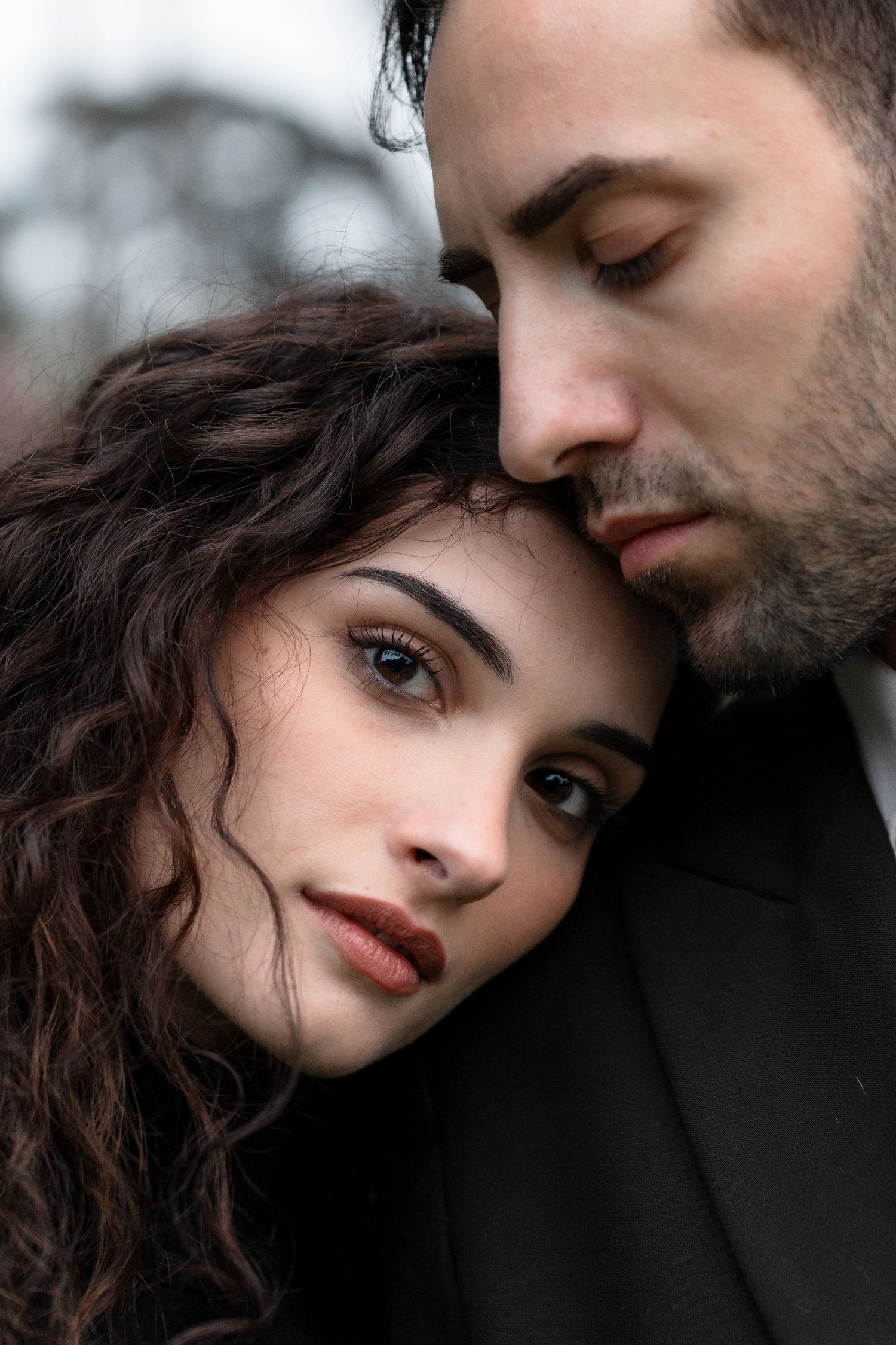 Intimate portrait of a couple in close embrace, with curly dark hair and dramatic lighting highlighting their features.