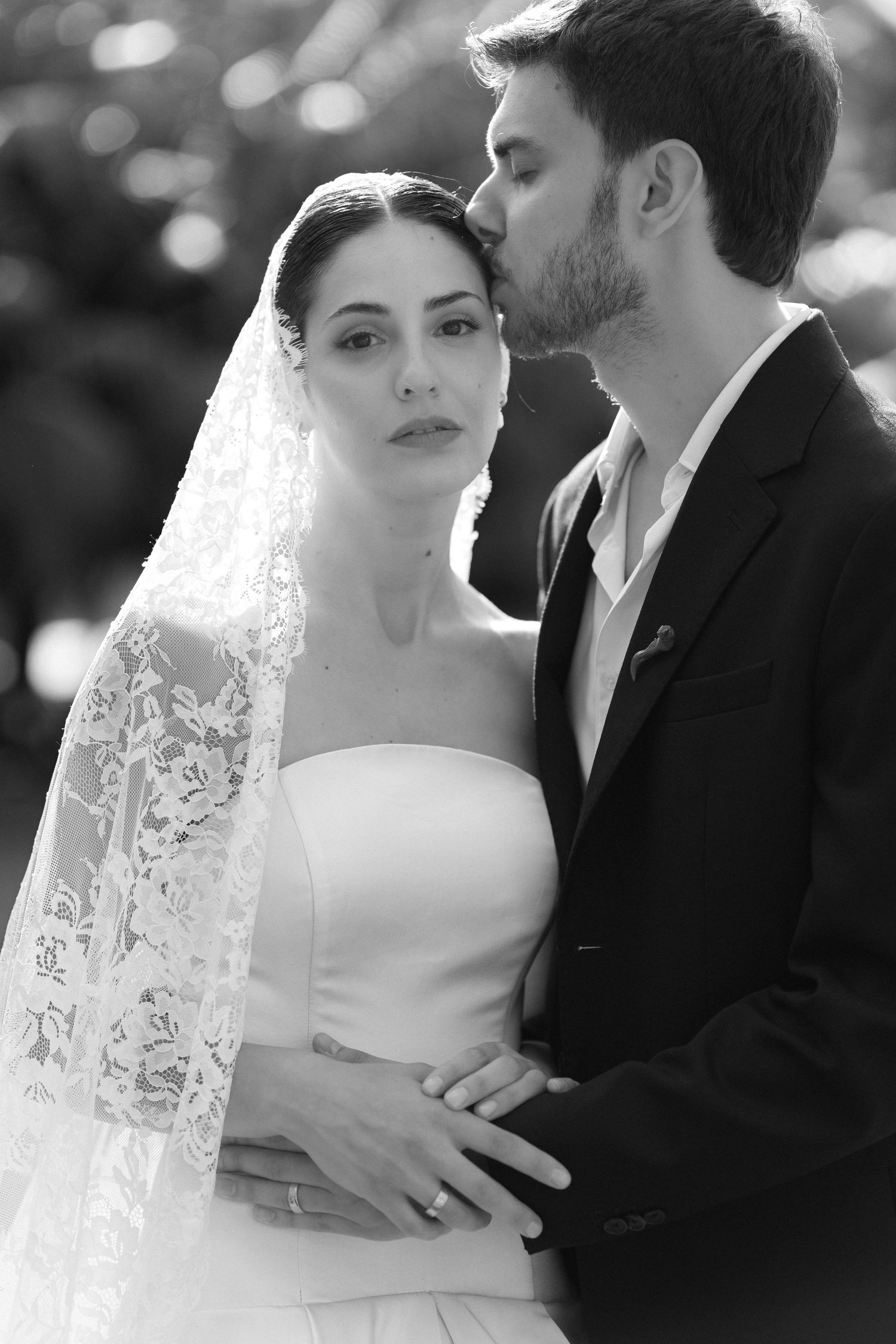 Black and white wedding photo of bride in lace veil and groom in suit sharing a tender moment.