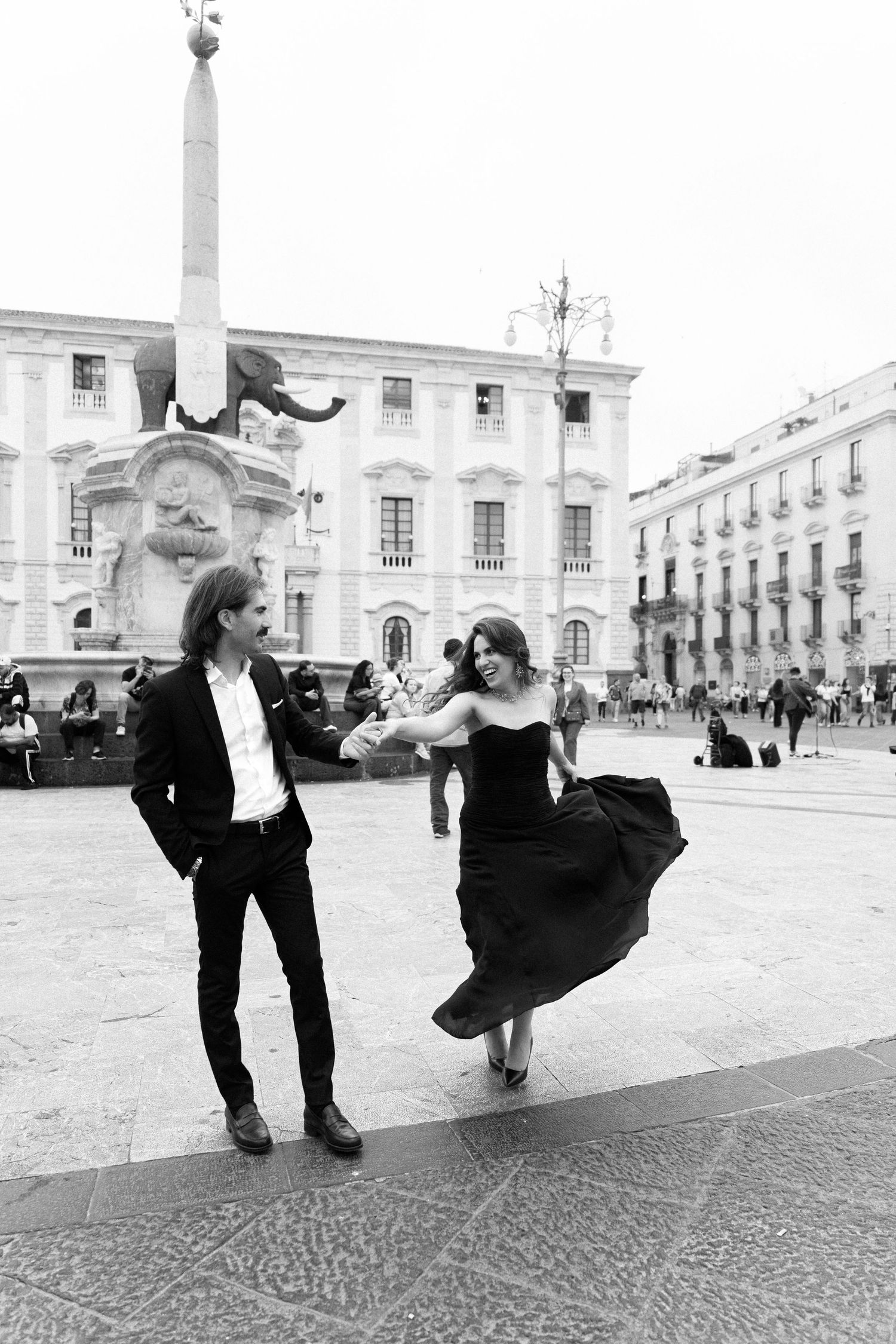 Couple dancing in black and white photo at Catania's Elephant Fountain square, woman in flowing dress, man in suit.
