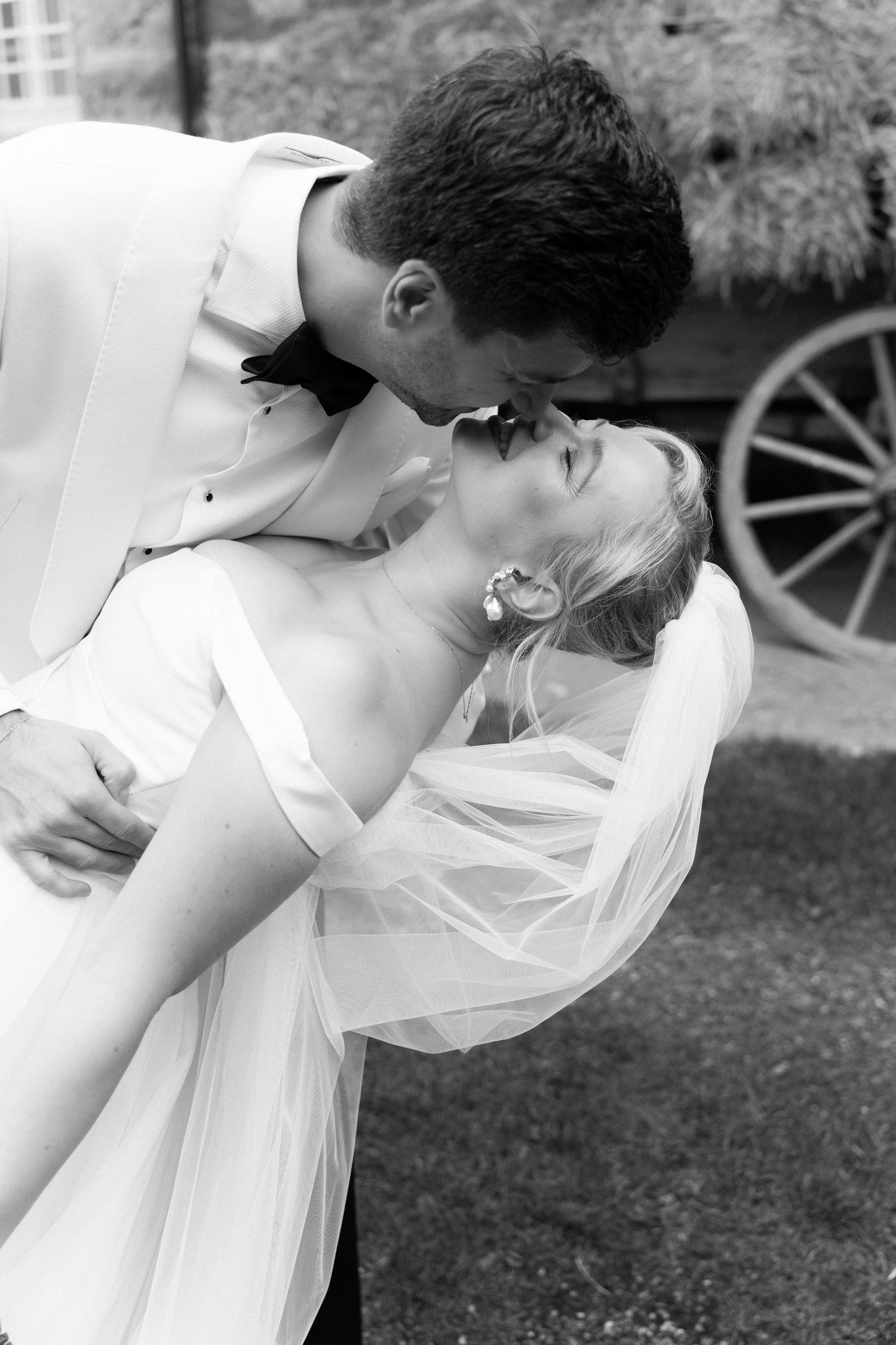 A romantic black and white wedding photo showing a couple in an intimate dip pose outdoors.