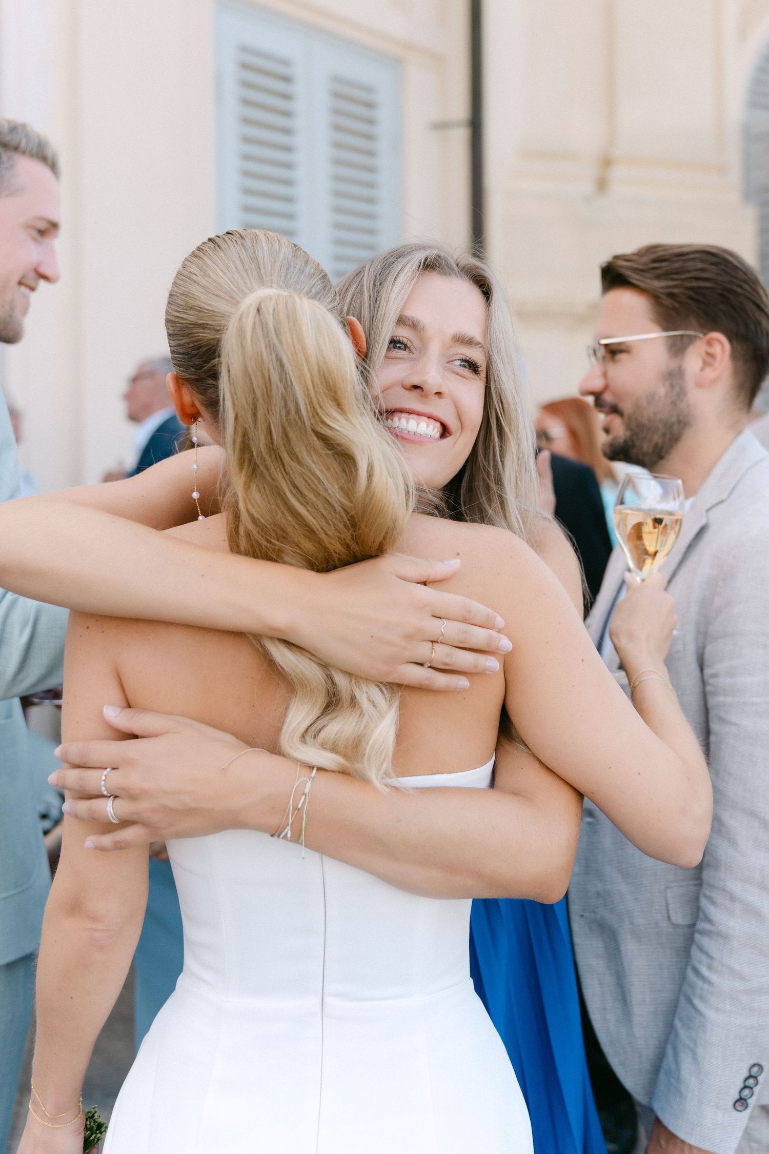 A series of candid wedding photos showing joyful hugs and embraces between guests at an outdoor celebration. Schloss Solitude