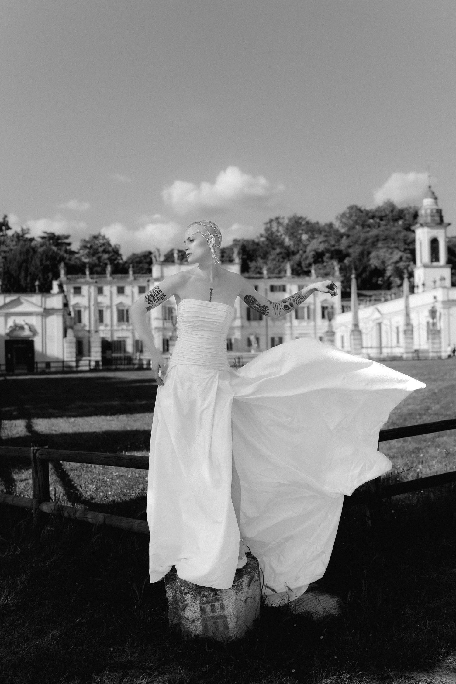 Black and white photo of a flowing white wedding dress against an elegant historic mansion backdrop with church spire.