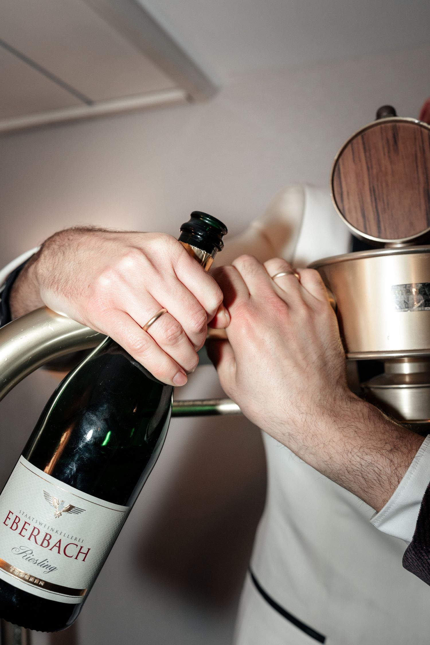Hands opening a bottle of Eberbach wine with a corkscrew against a light background.