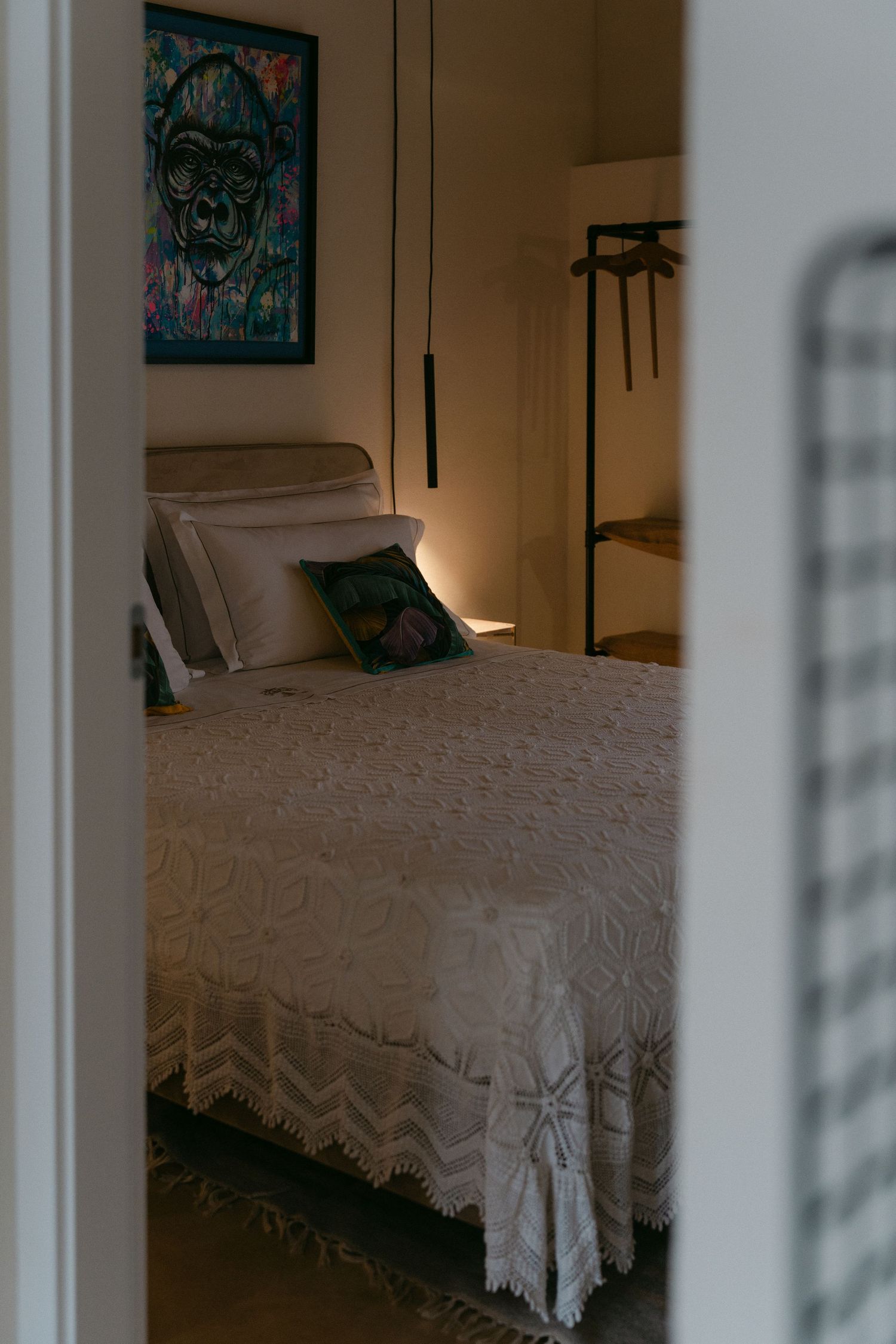 Bedroom interior with white bedding and blue-green artwork viewed through doorway.