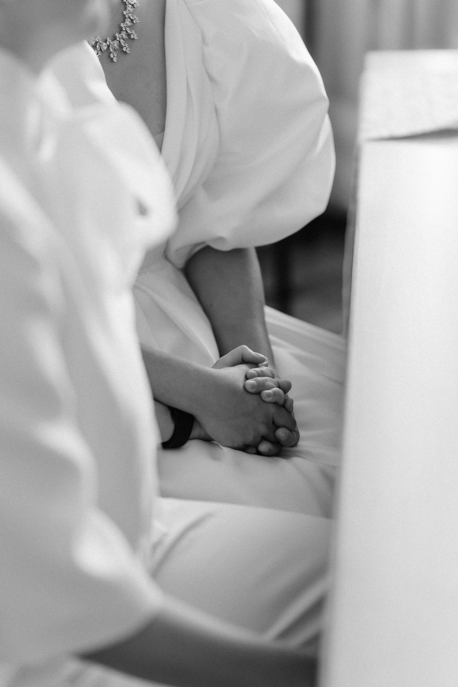 Black and white photo of a couple holding hands in wedding attire, seated together during a ceremony.