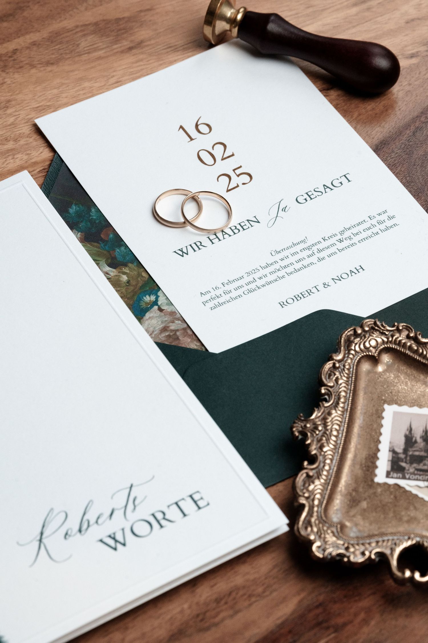 Wedding stationery with rings, date numbers and ornate frame showing elegant save the date details on wooden surface.