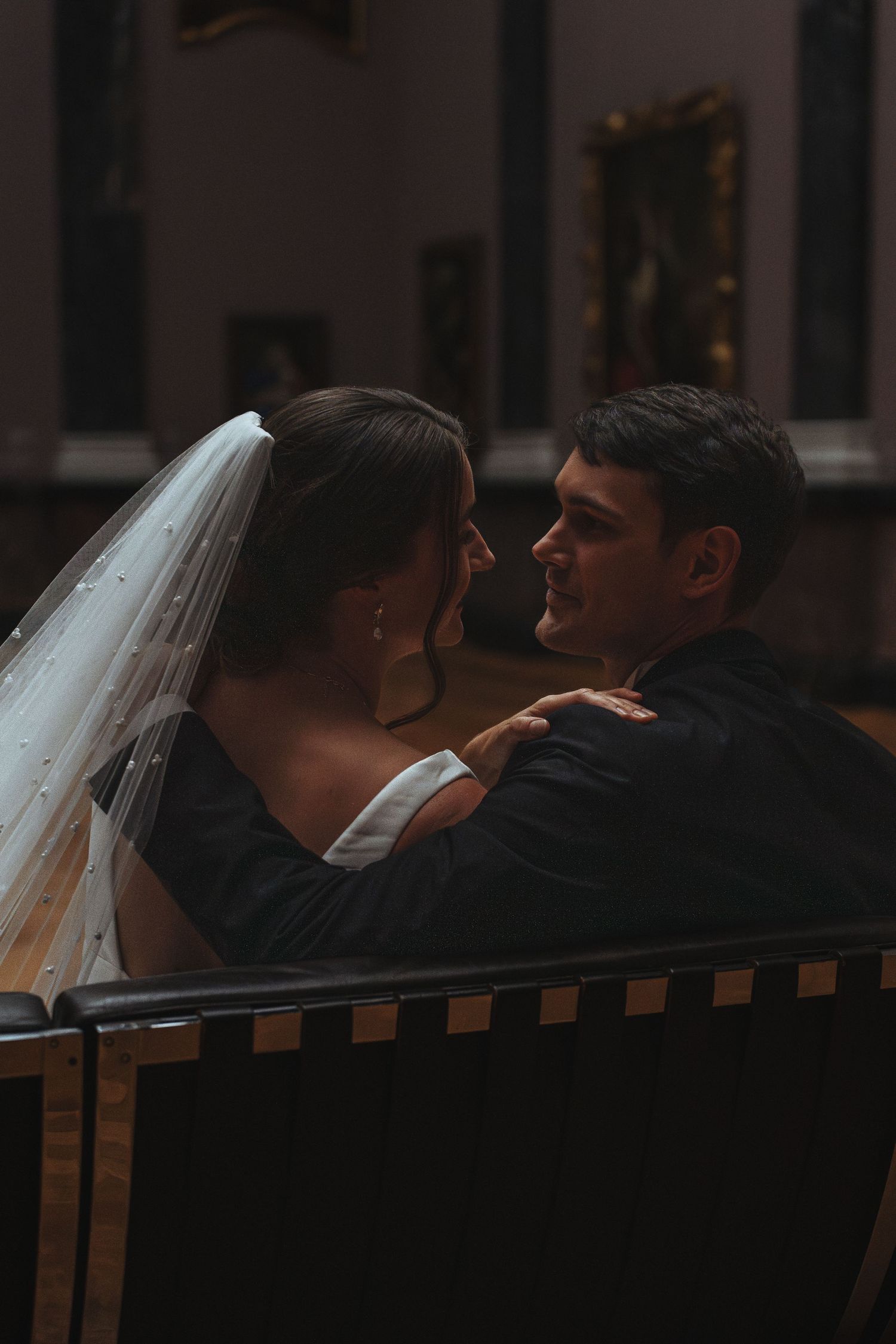 A romantic wedding couple sharing an intimate moment while sitting together in a dimly lit setting.