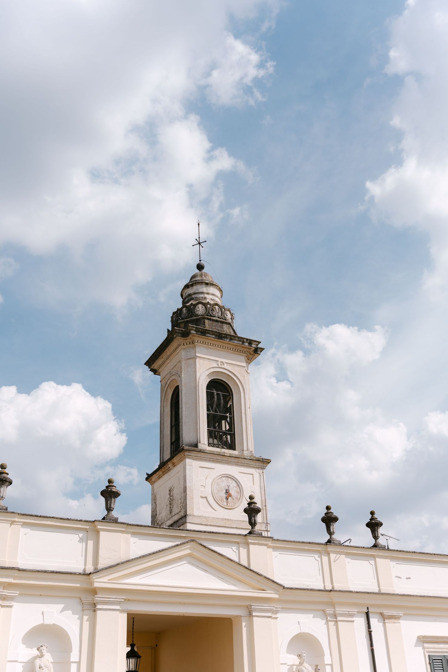 White church facade with bell tower and ornate crosses against a blue cloudy sky in classical architectural style. Villa Mosconi Bertani