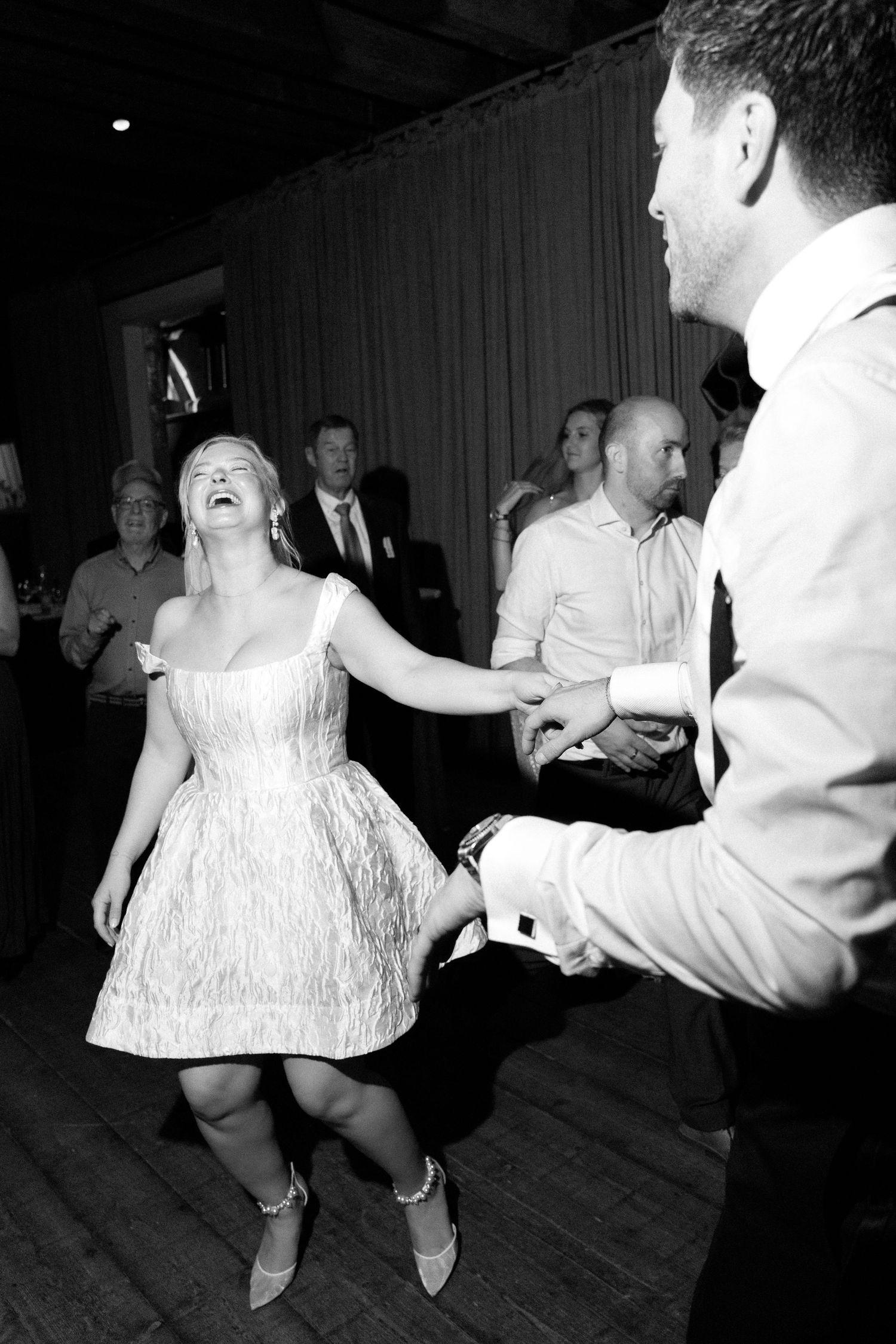 A person in a white dress spins and dances on a wooden dance floor during what appears to be a celebration.