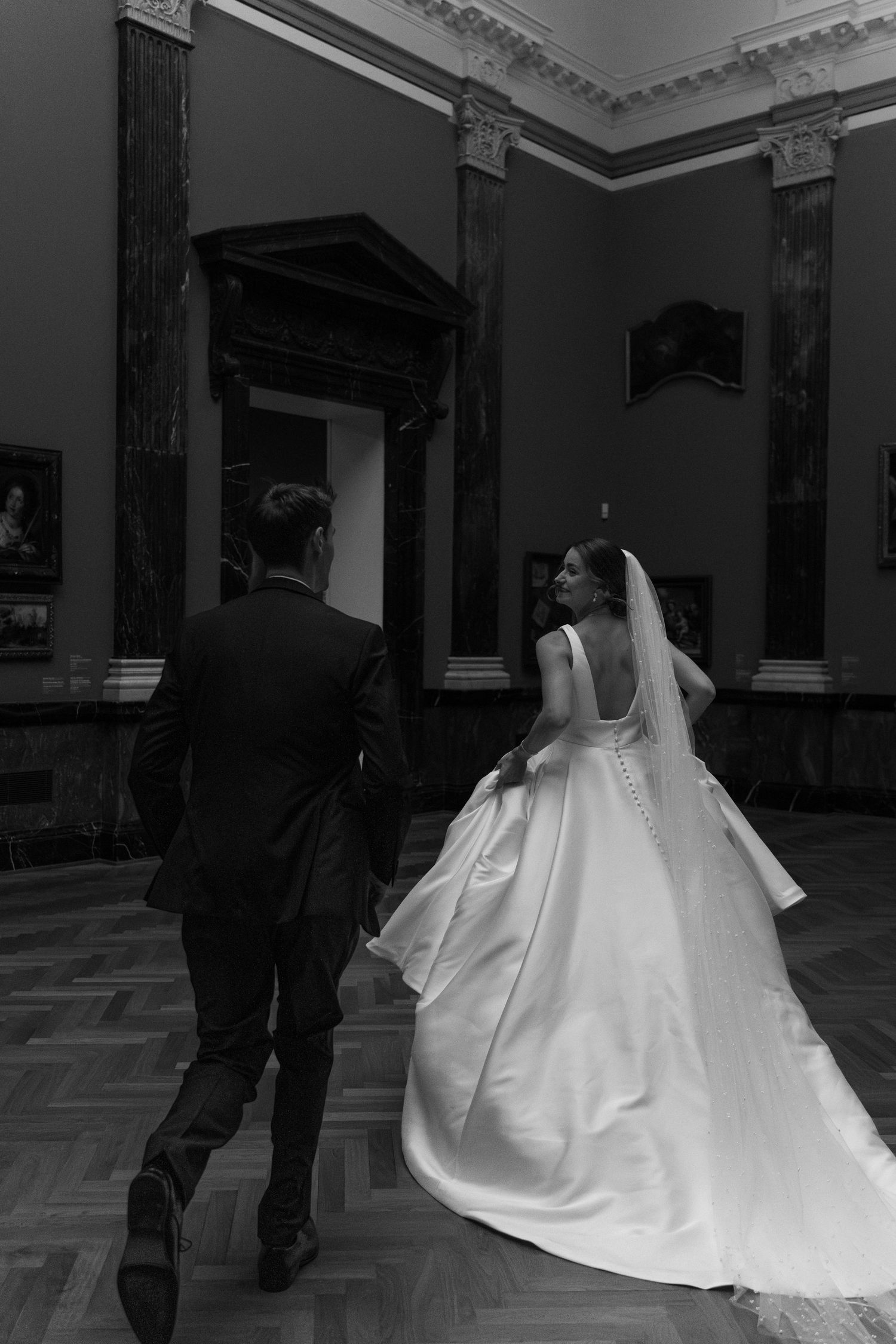 A black and white photo series showing a bride in a flowing white gown walking with a suited figure in an elegant hall.