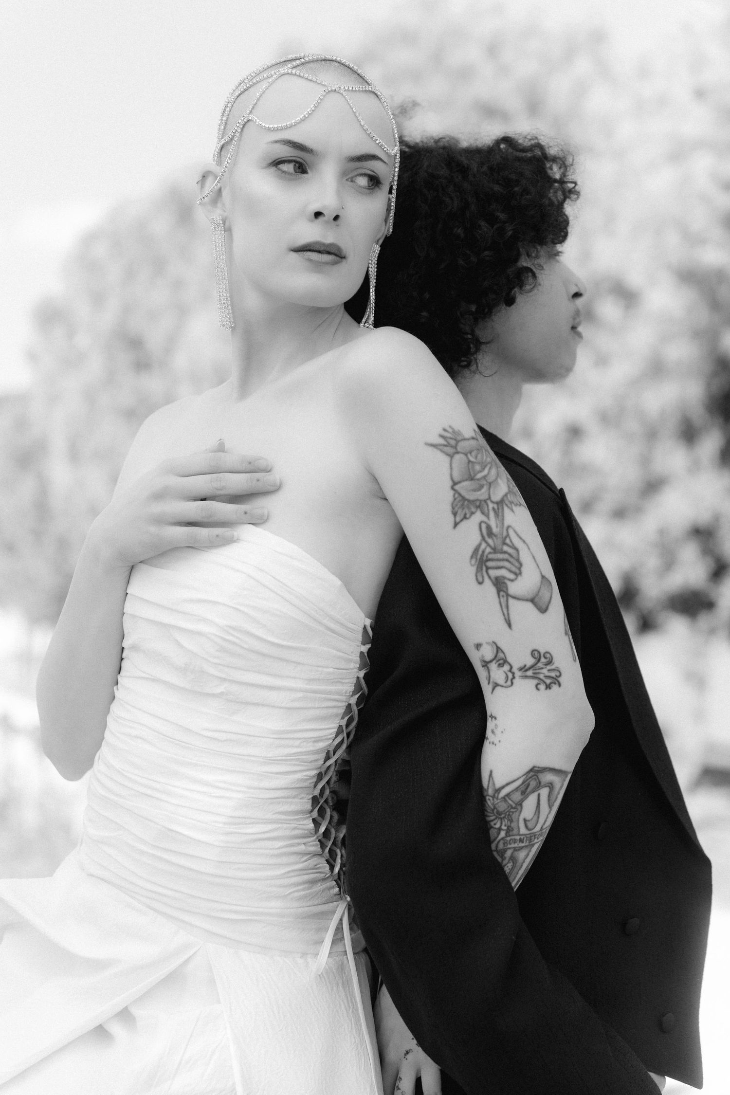 Black and white artistic portrait of a couple in contrasting wedding attire showing tattoos and elegant styling.