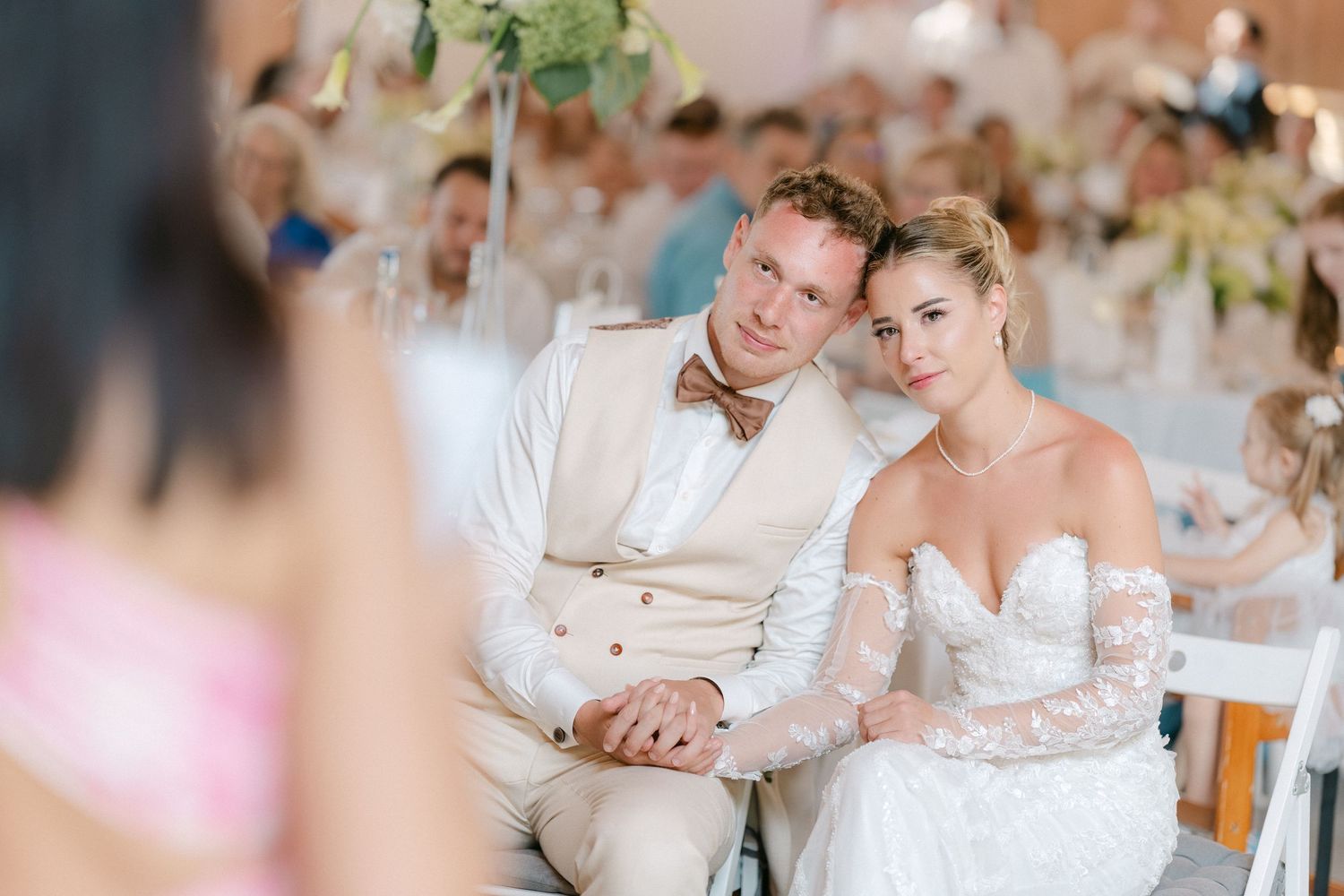 A couple shares an intimate moment during their wedding reception while seated at a white-decorated table.