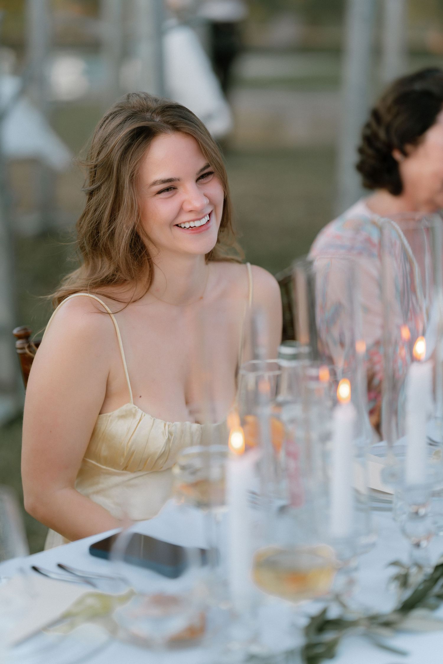 Smiling young woman in gold dress at candlelit wedding reception table.