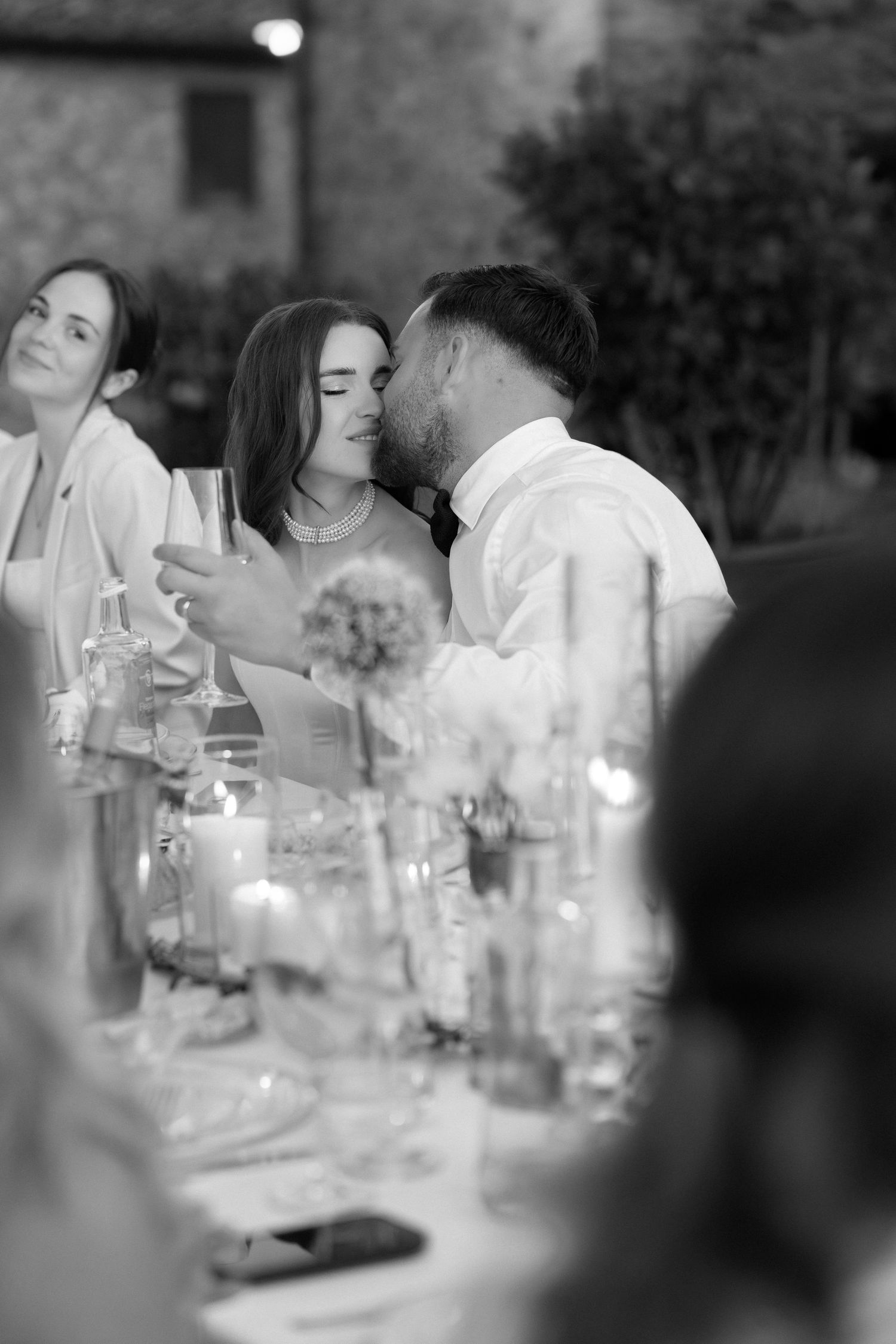 Black and white photo of a couple sharing a kiss at an elegant outdoor wedding reception dinner table.