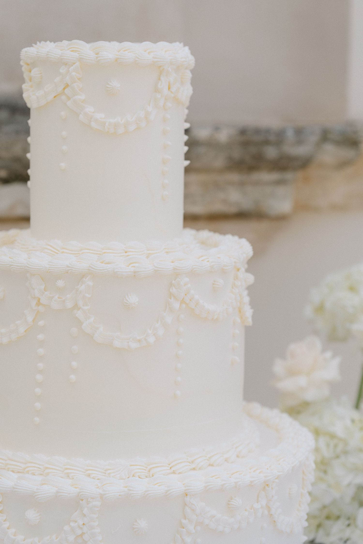 Elegant white wedding cake decorated with delicate piped pearls and lace details in a classic tiered design. Villa Mosconi Bertani