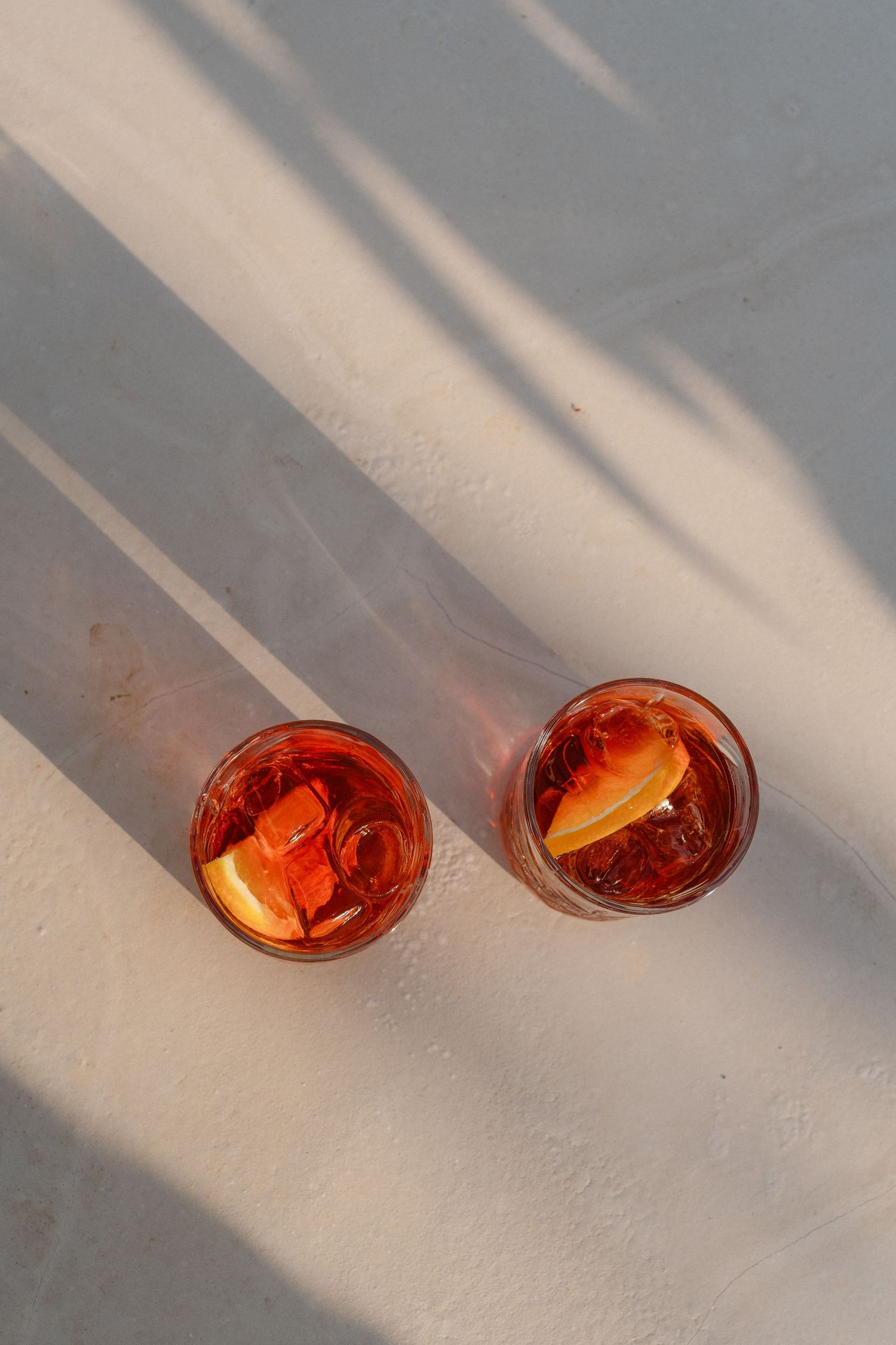 Three orange-colored cocktails casting shadows on a white surface.