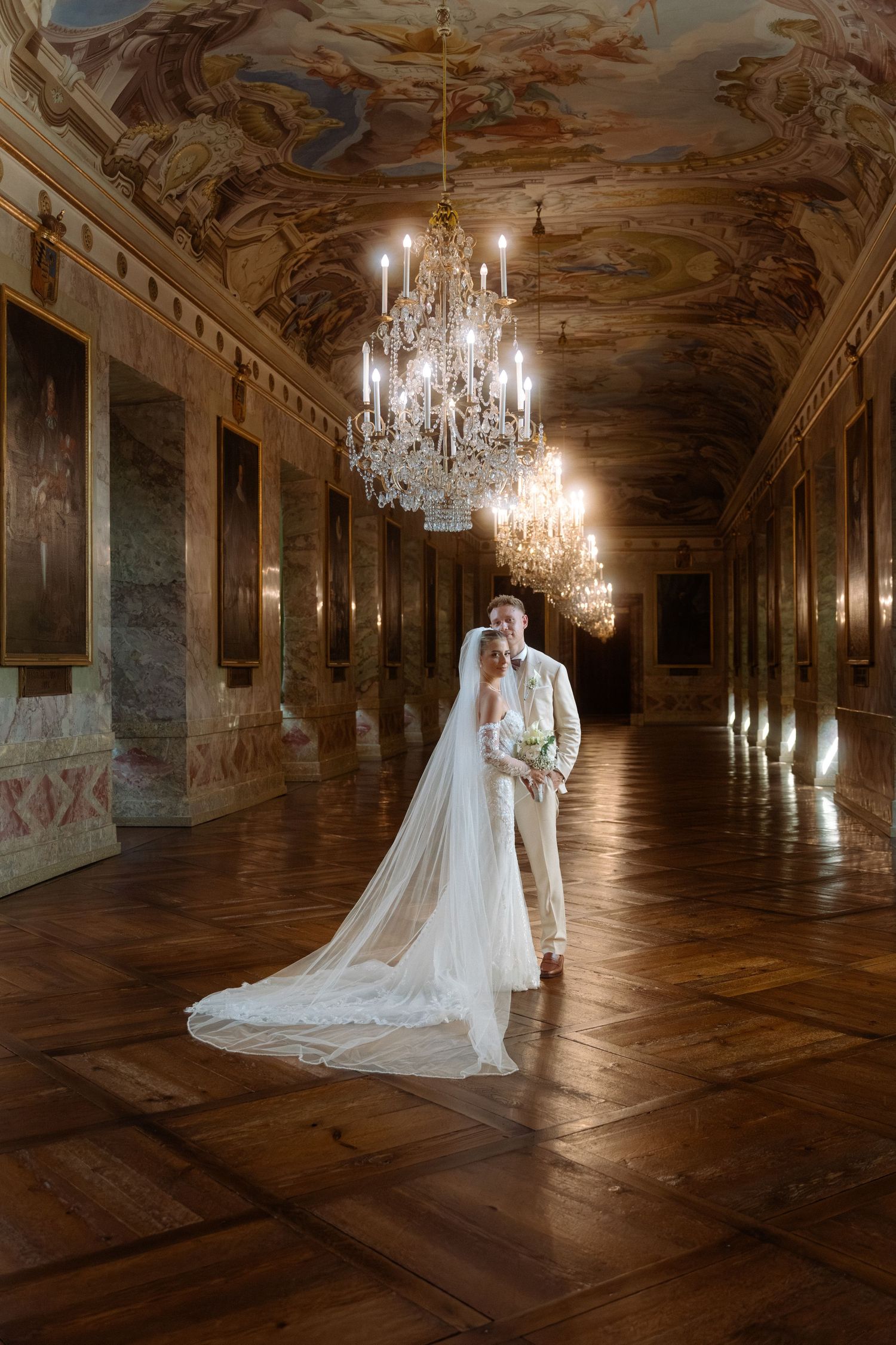 Elegant bridal portrait in a grand palace hallway with ornate chandeliers and baroque painted ceilings. Schloss Ludwigsburg