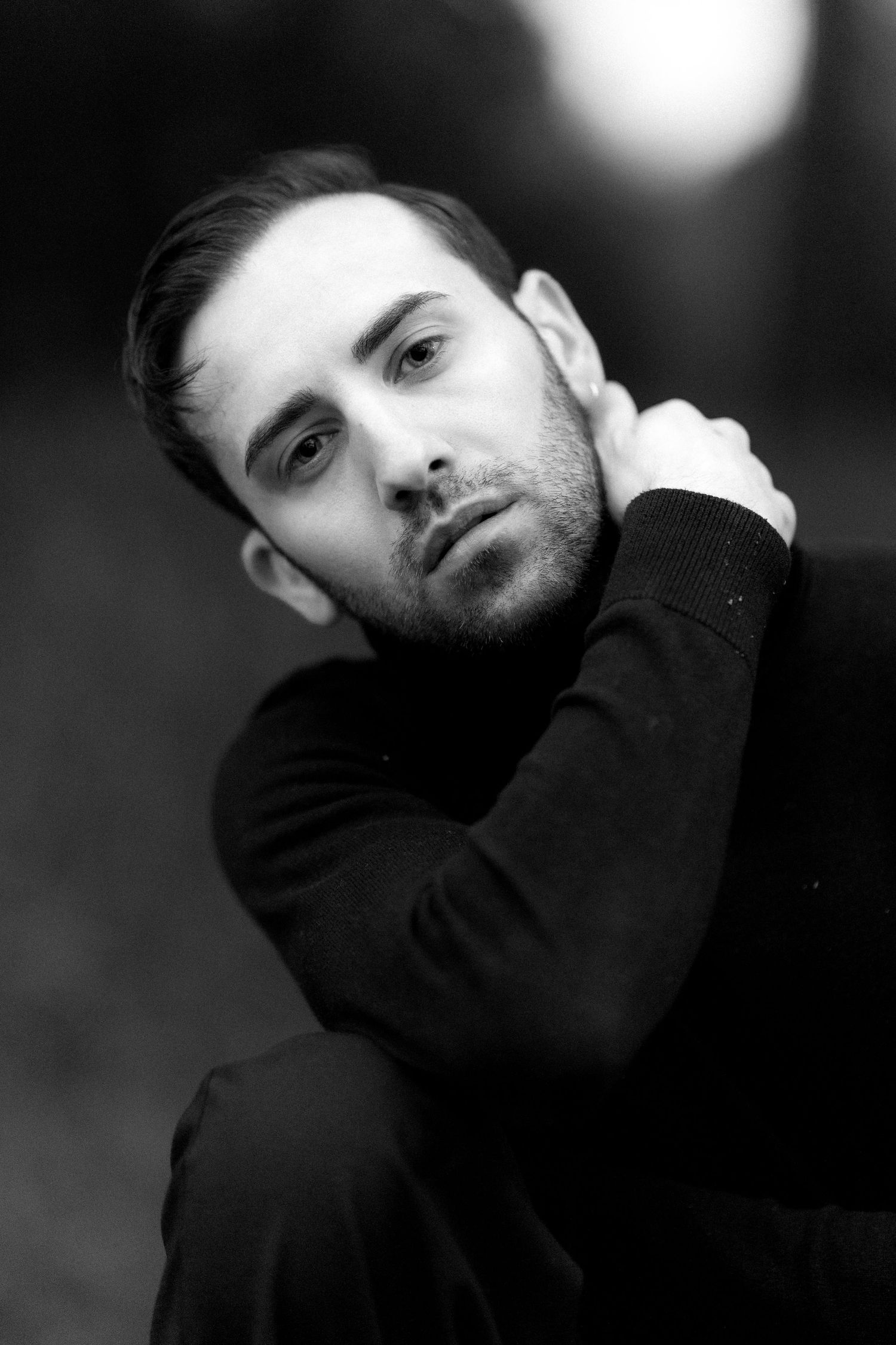 Artistic black and white portrait of a person in a black sweater with a contemplative expression against a blurred background.