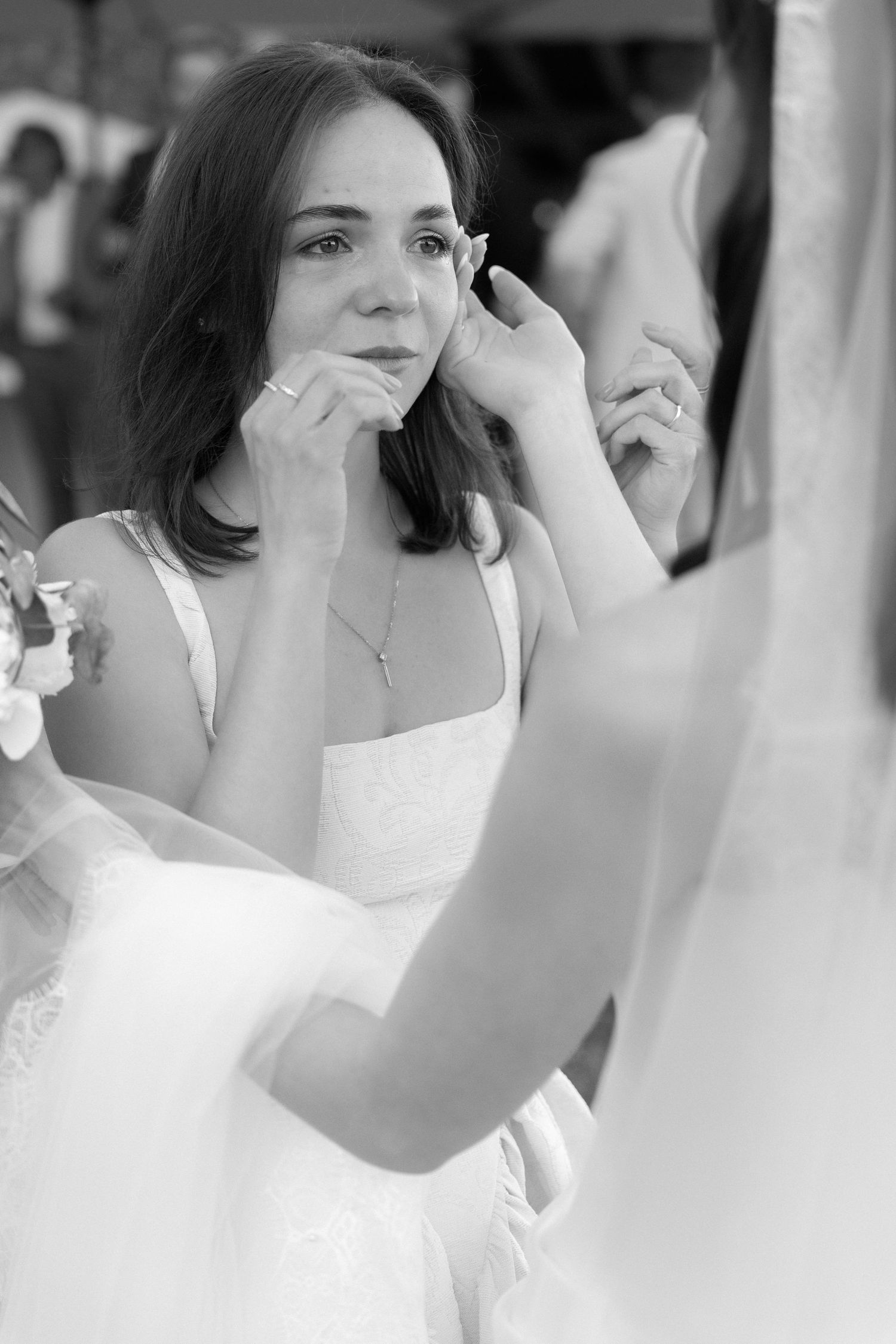 Black and white photo of an emotional bride wiping tears while looking in a mirror on her wedding day.