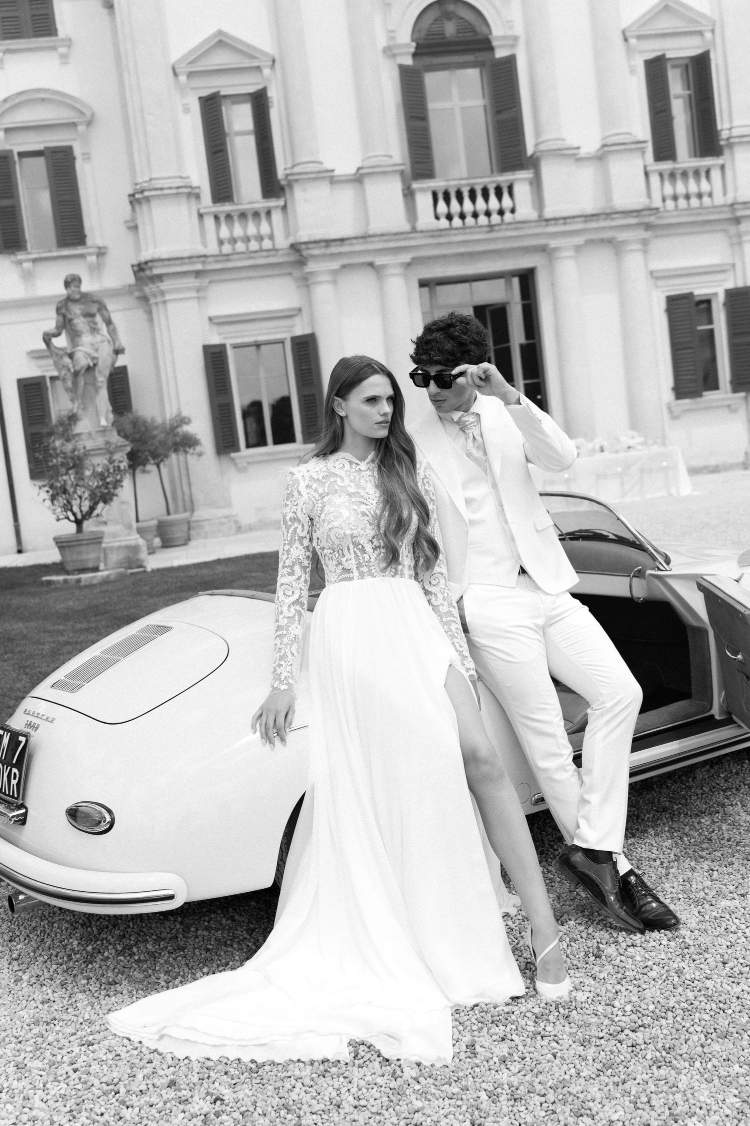 A black and white photo series showing a bride in a lace wedding dress posing with a vintage white sports car. Villa Mosconi Bertani