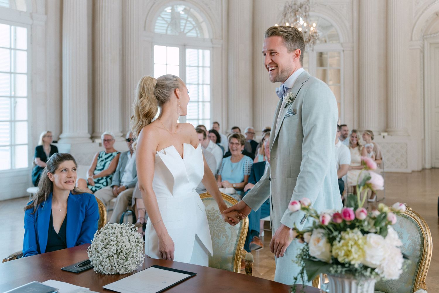 Newlyweds share their first dance in an elegant white ballroom with guests watching from the sidelines. Schloss Solitude