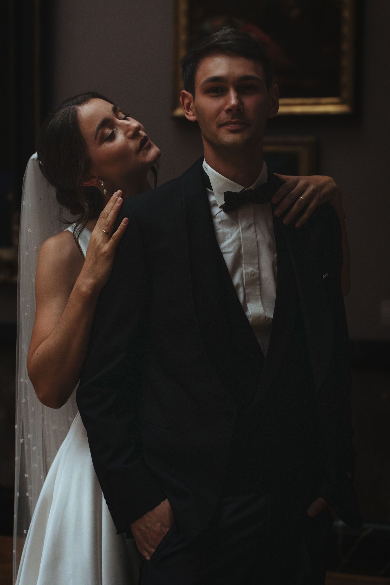 Moody wedding portrait of a bride and groom in dark elegant setting with dramatic lighting.