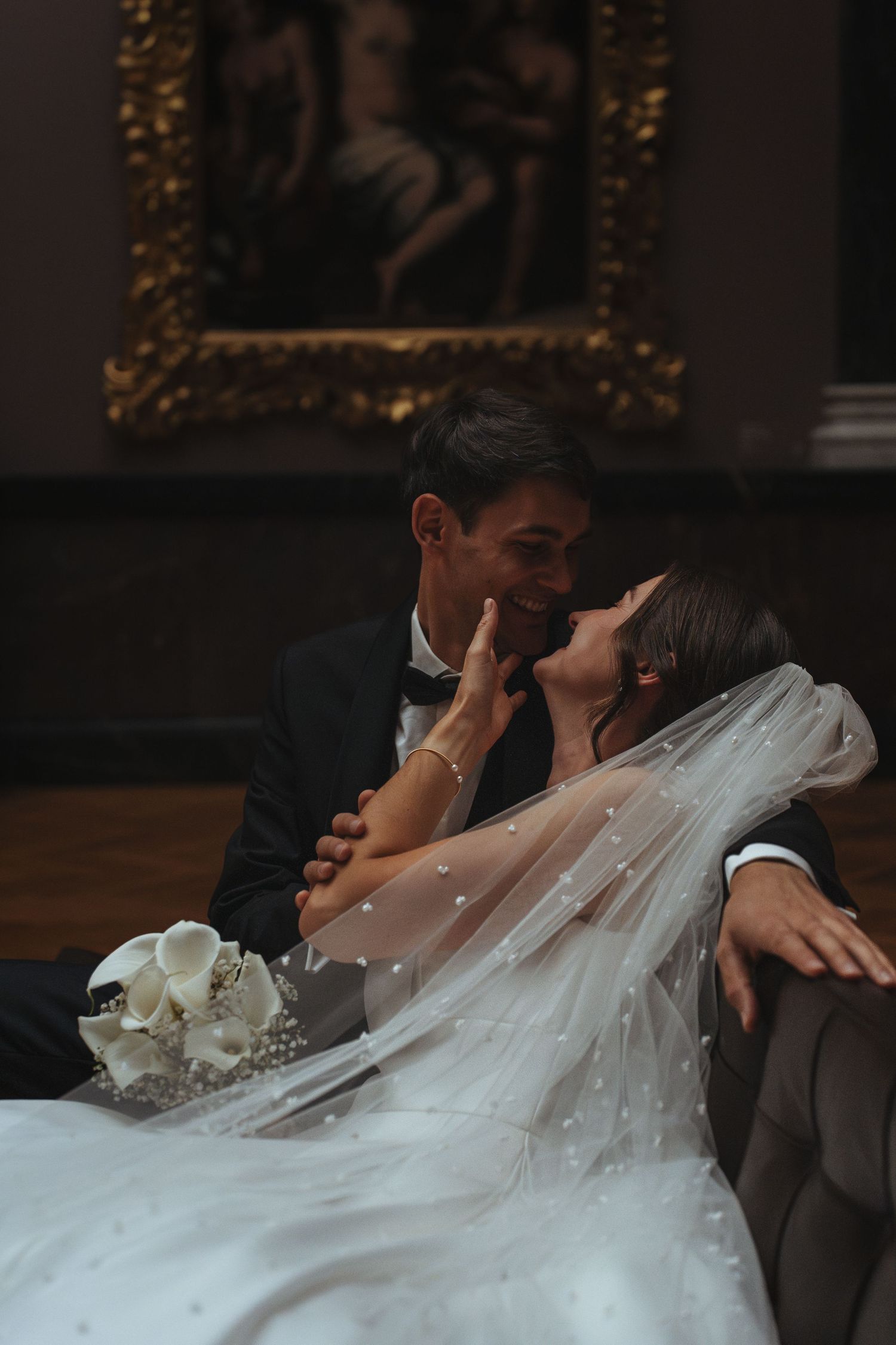 A romantic wedding couple shares an intimate kiss in a dimly lit venue with ornate decorations.