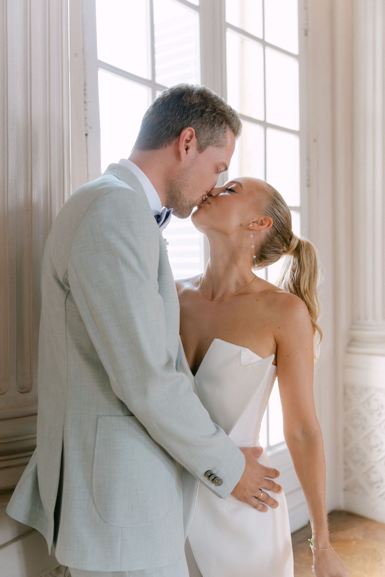 A romantic wedding moment with a couple sharing a tender kiss by a sunlit window. Schloss Solitude