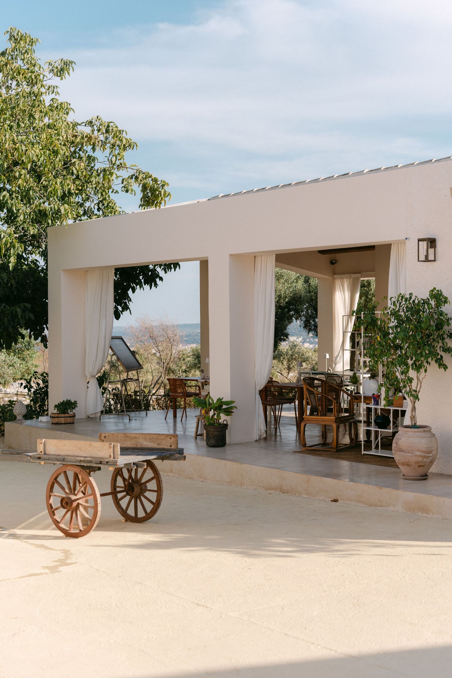 Elegant outdoor terrace with white columns and vintage cart overlooking a scenic landscape.