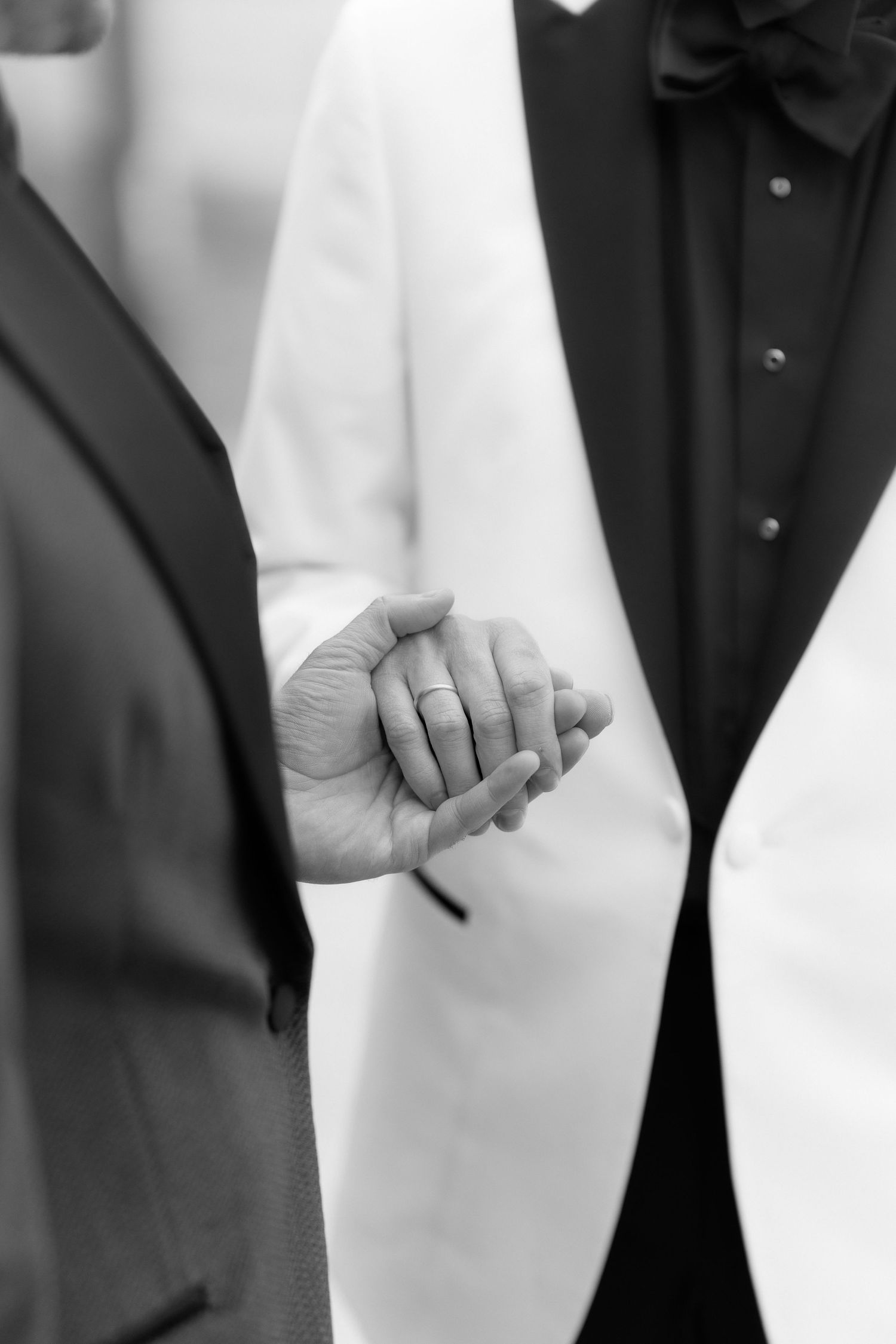 A black and white close-up photo shows two hands joined, with a wedding ring visible, symbolizing marriage and commitment.