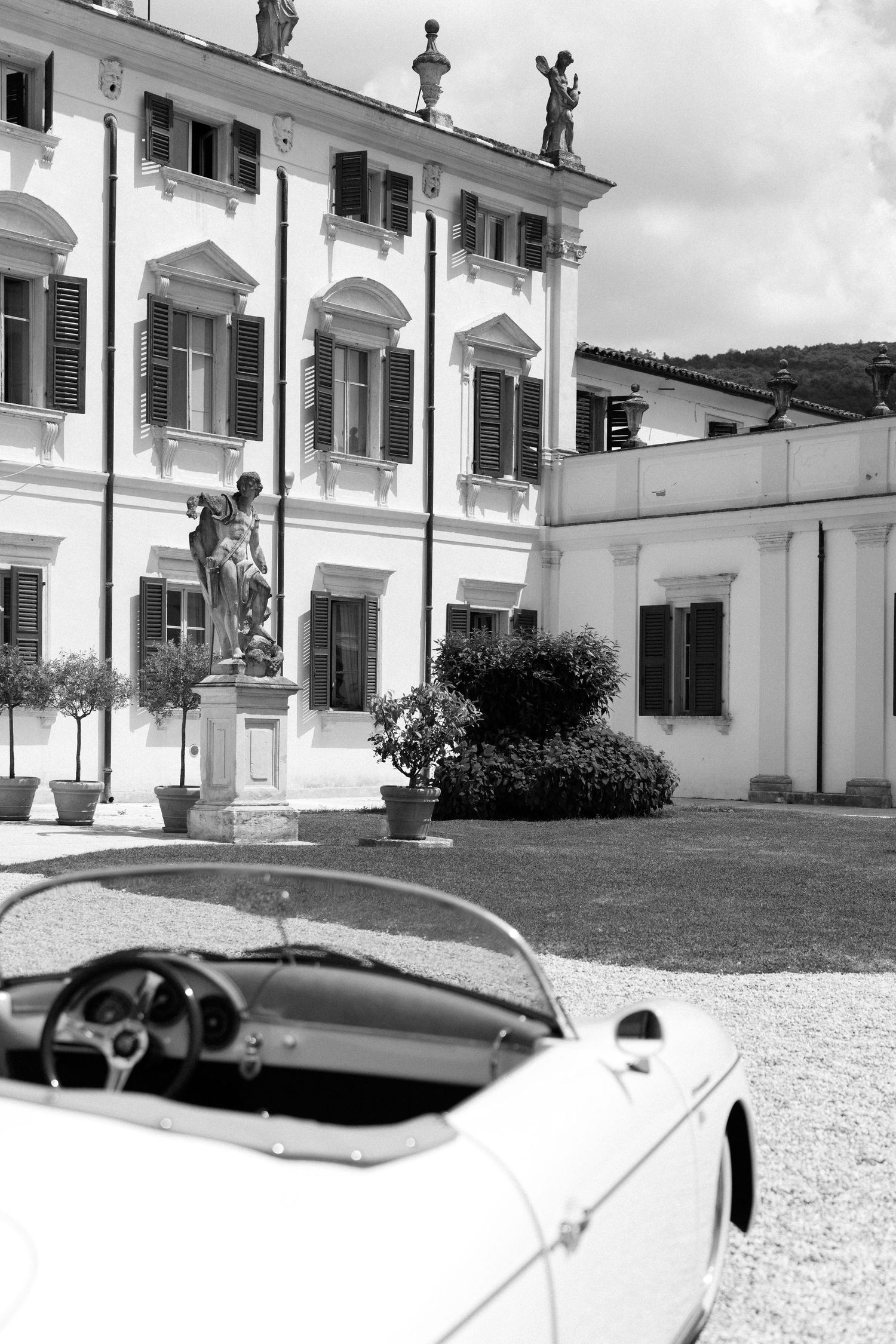 A classic white convertible car parked in front of an elegant white colonial-style building with shuttered windows. Villa Mosconi Bertani