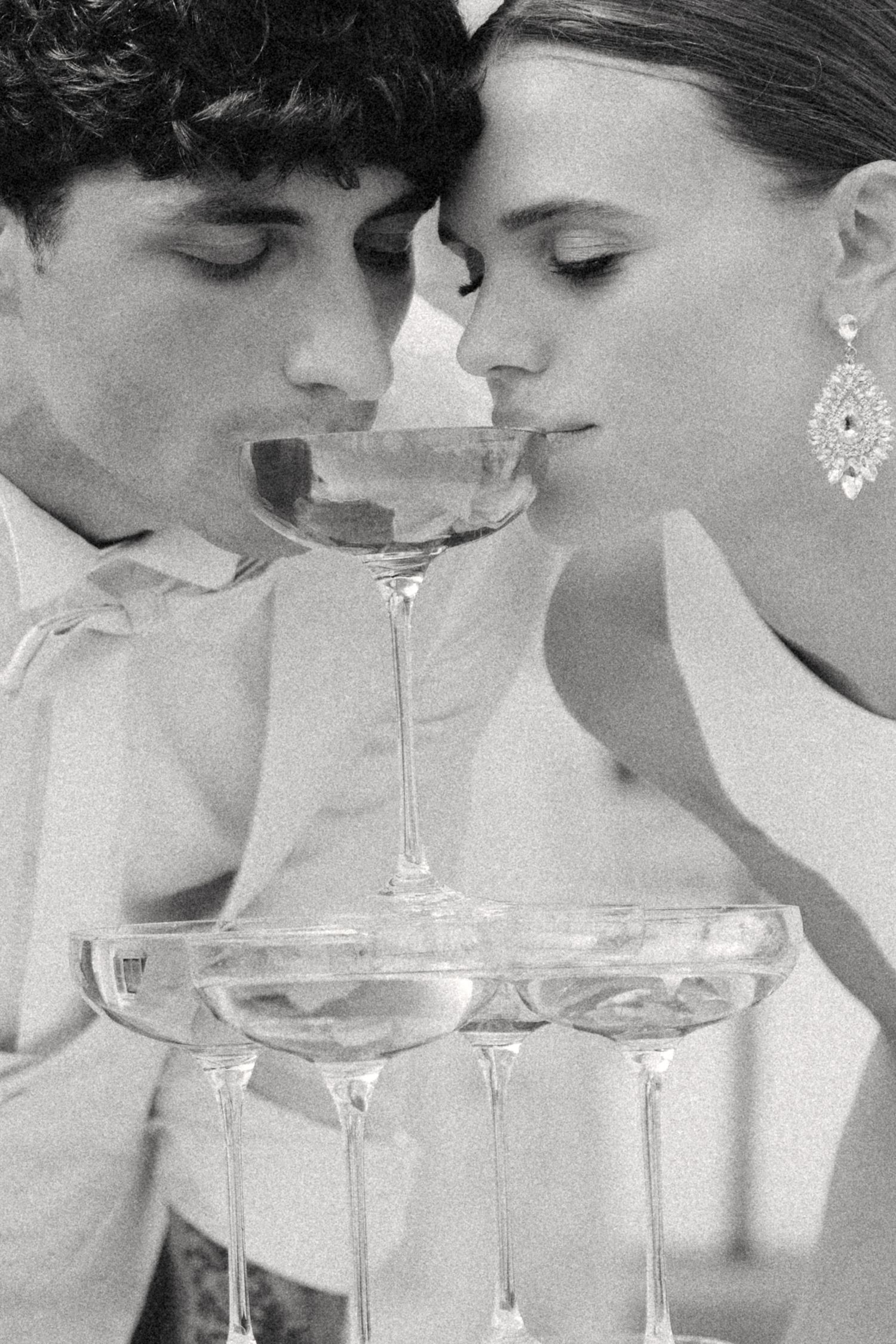 A black and white photograph showing a champagne tower being built with crystal glasses stacked in layers. Villa Mosconi Bertani
