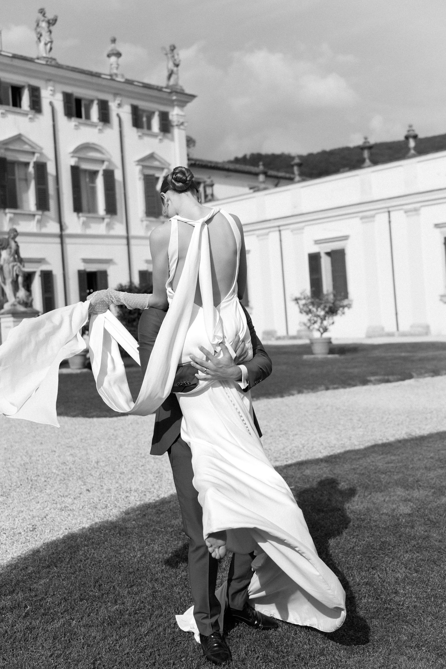 Black and white photo of a couple dancing outdoors at an elegant villa with white flowing dress in motion. Villa Mosconi Bertani