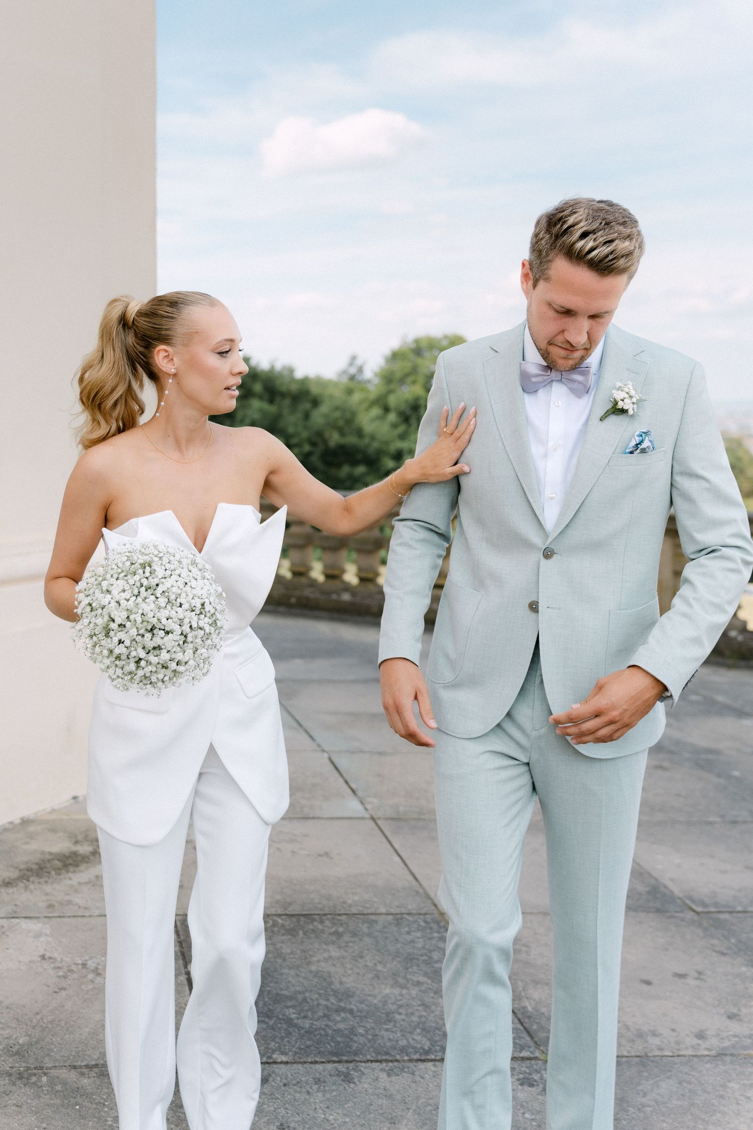 A couple in wedding attire shares playful moments during a photoshoot on a concrete surface outdoors. Schloss Solitude