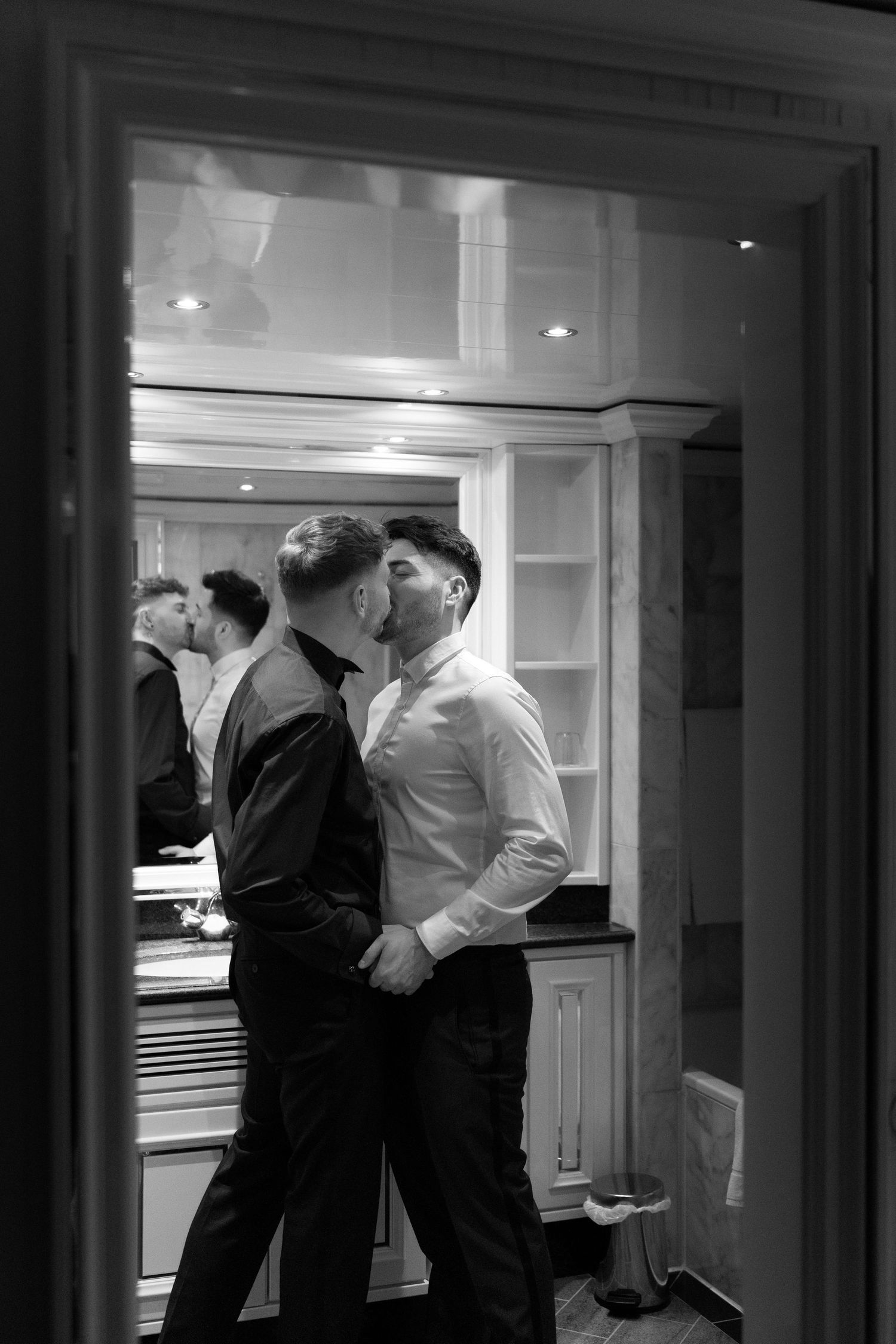 A couple embraces in an intimate moment, captured in black and white through a doorway interior.