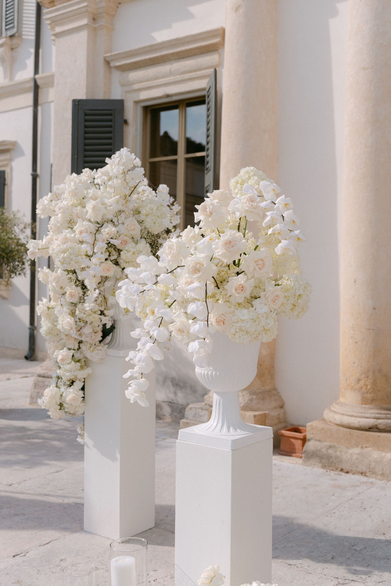 Elegant white floral arrangements in classical urns decorate a Mediterranean-style building entrance.
