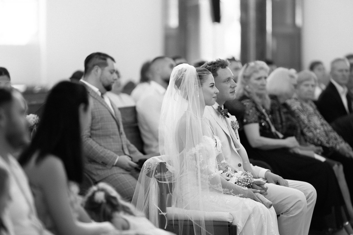 Wedding guests seated in rows watching an emotional ceremony at an indoor venue.