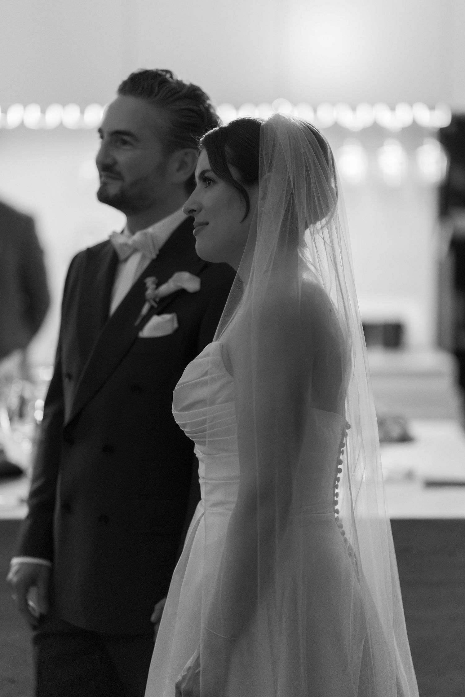 Black and white photo of a smiling bride in veil and groom in suit standing together during wedding ceremony.