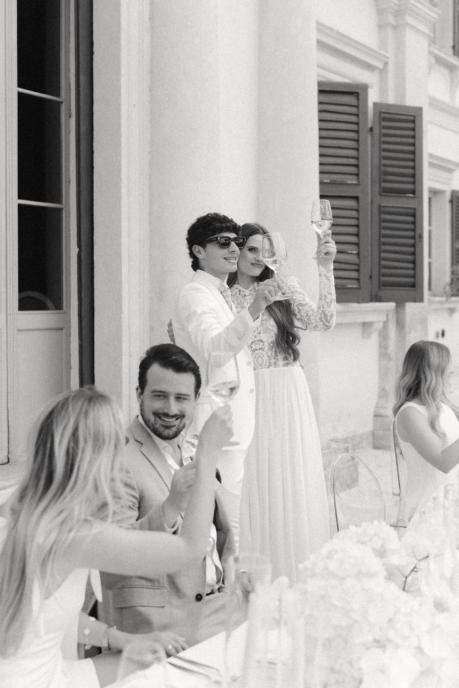 A group of people dressed in white gather together at an elegant venue with shuttered windows and white decor. Villa Mosconi Bertani