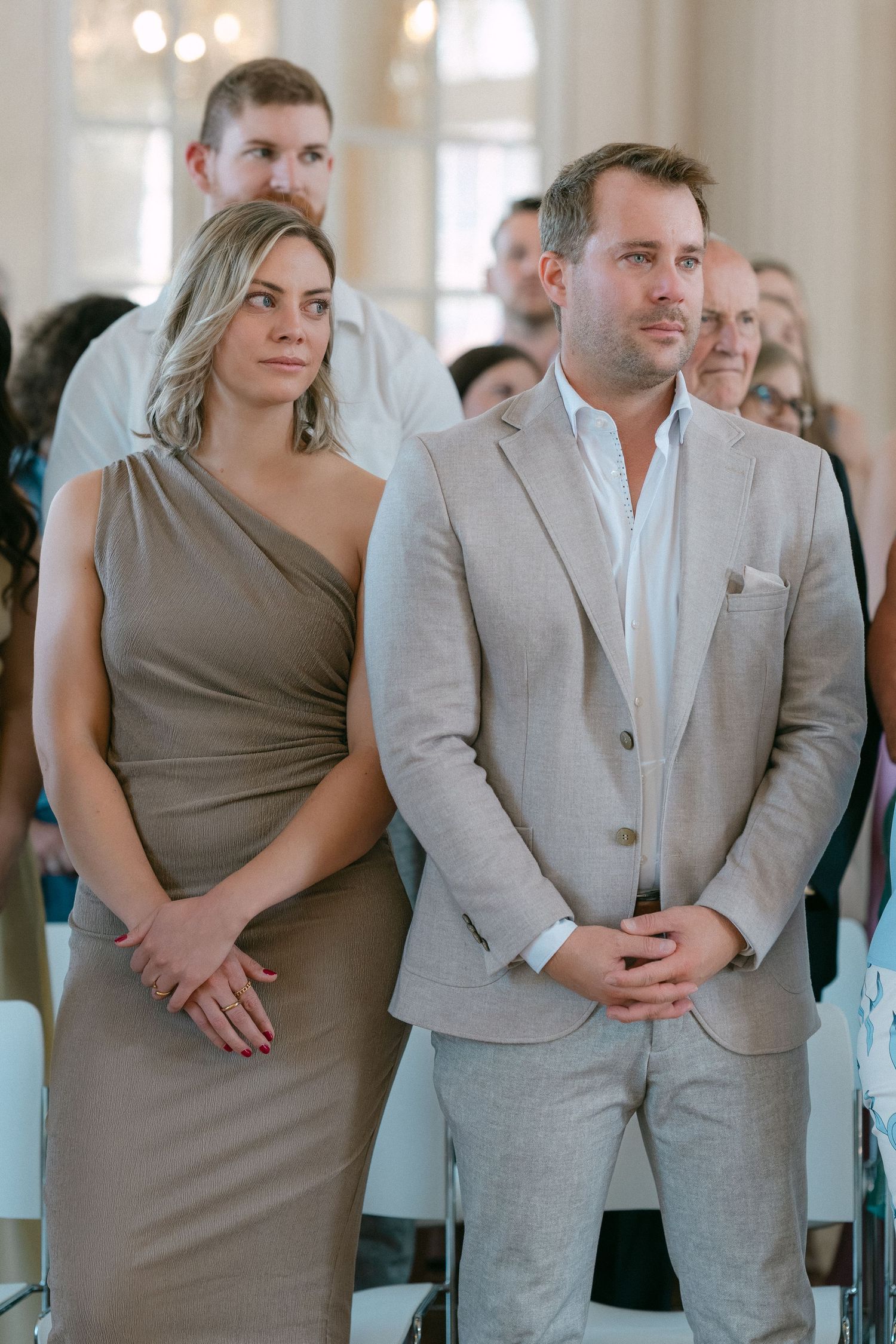 A couple in coordinating gray and taupe attire stands together during what appears to be a formal event. Schloss Solitude