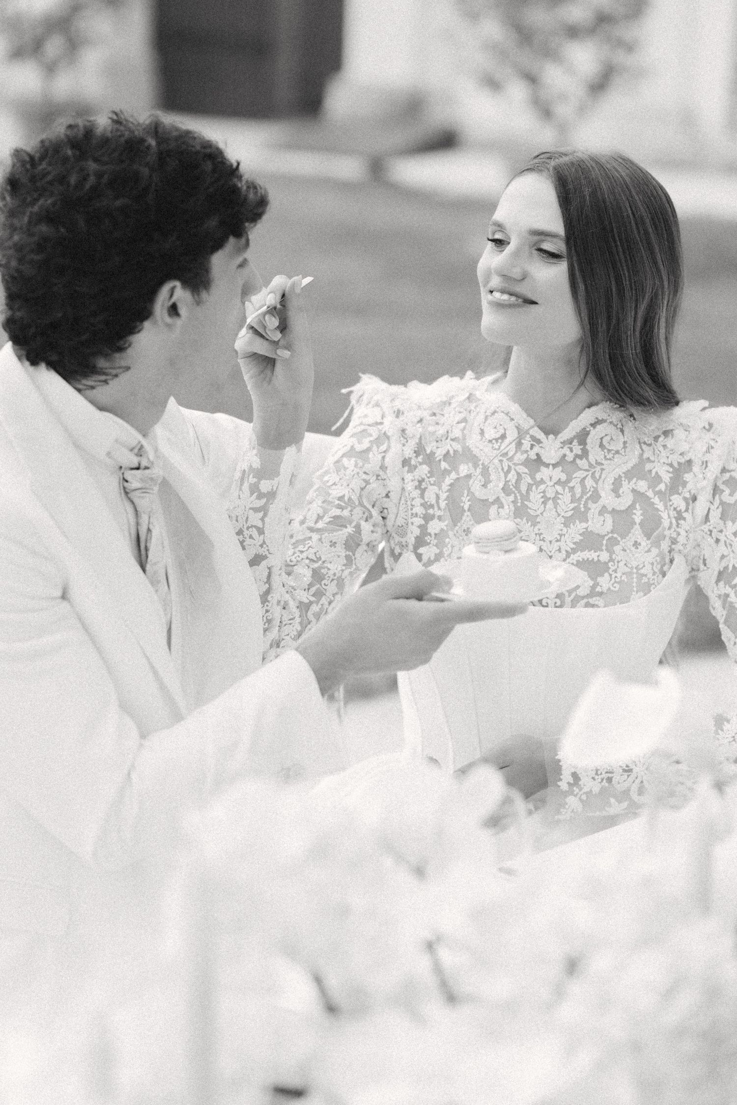 A black and white photo of a couple in white attire sharing a sweet moment during their wedding celebration. Villa Mosconi Bertani