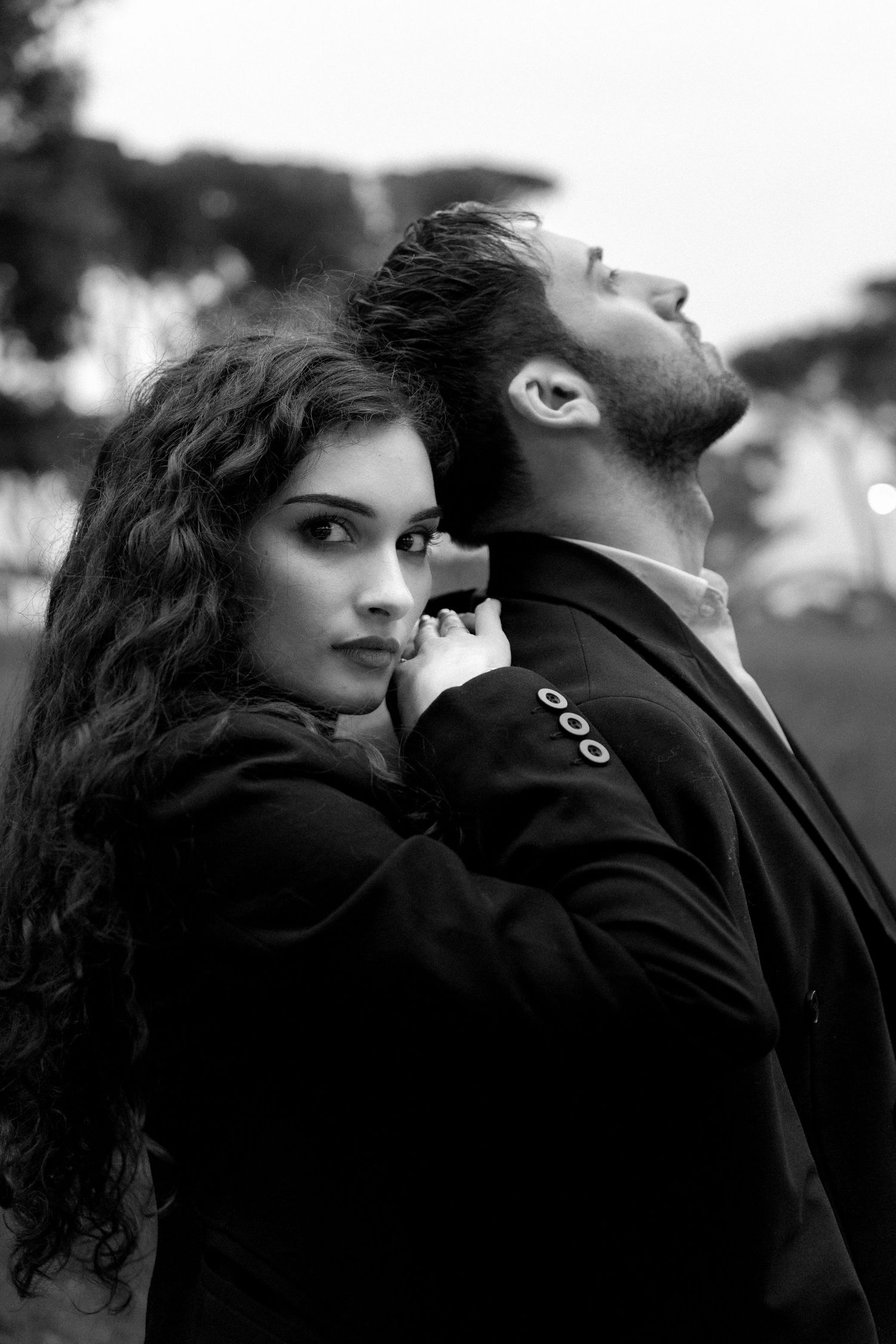 A dramatic black and white portrait of a couple in romantic poses against a blurred outdoor background.